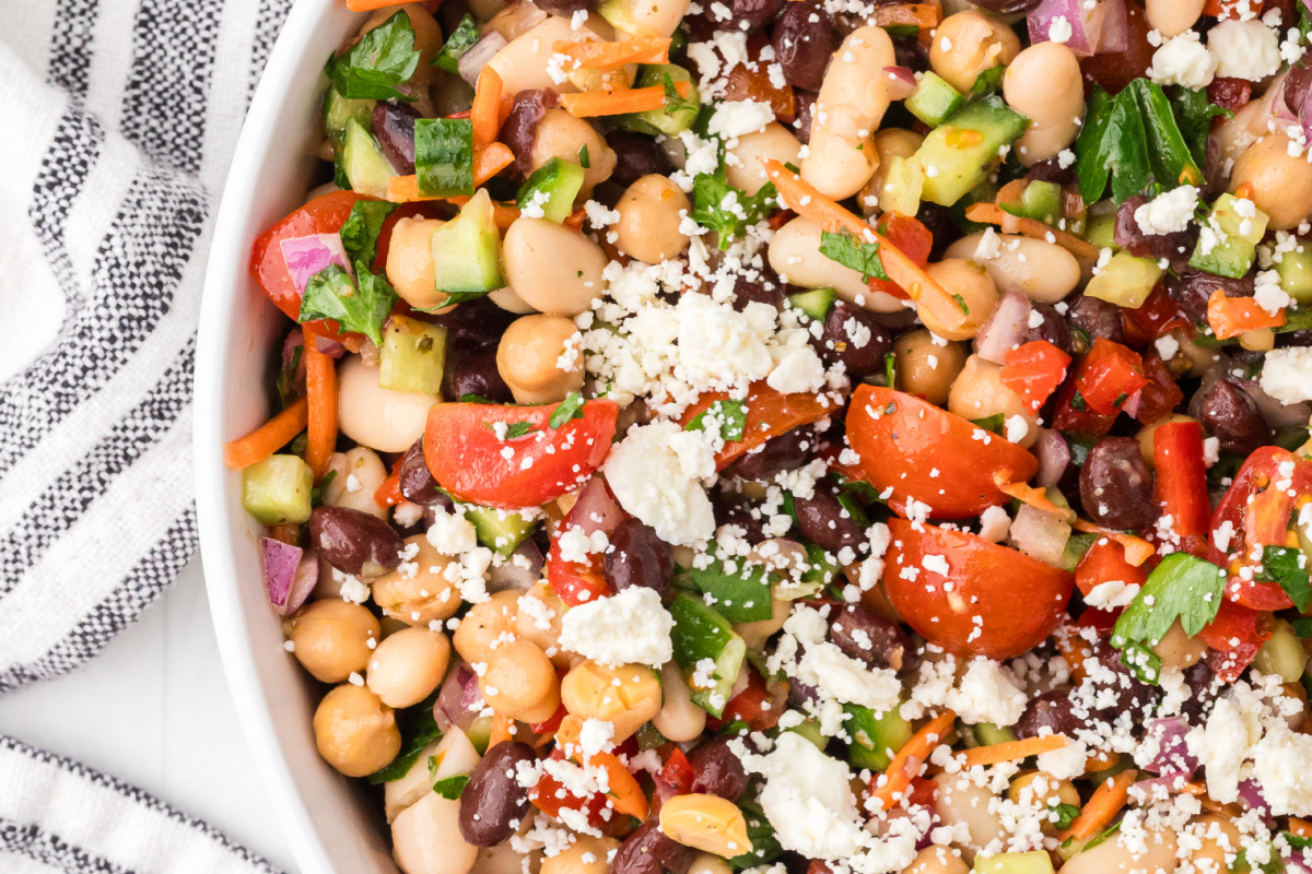 Close-up of high protein dense bean salad with feta cheese, chopped vegetables, and three kinds of beans tossed in lemon Dijon dressing. High protein dense bean salad with chickpeas, black beans, cannellini beans, feta cheese, tomatoes, cucumber, and parsley