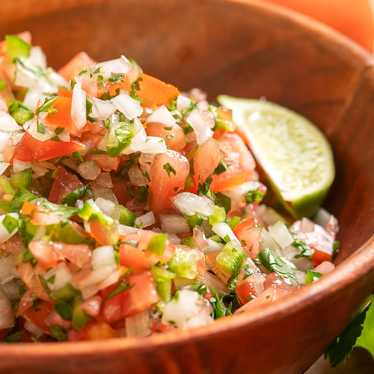 Homemade pico de gallo served in a wooden bowl with fresh lime and cilantro
