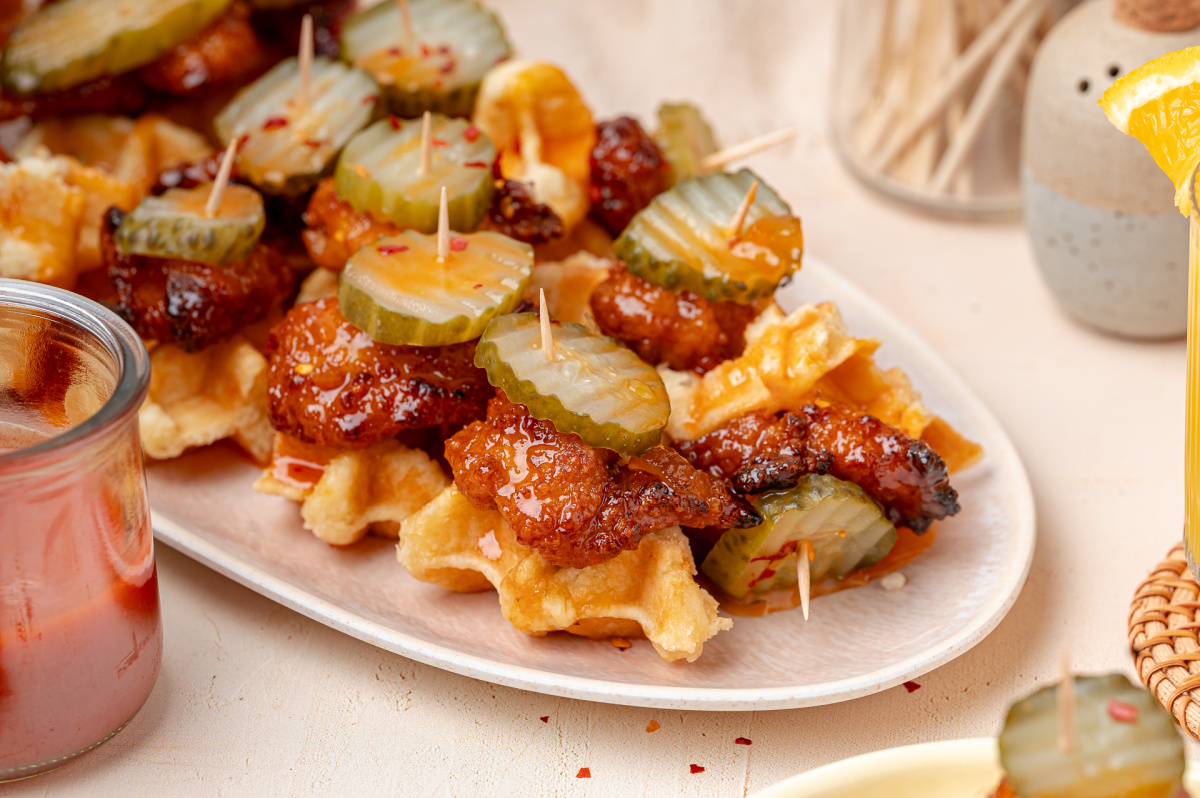 Hot Honey Peach Chicken and Waffle Bites Party Platter Hot honey peach chicken and waffle bites arranged on a platter with dill pickle chips and peach hot honey glaze.
