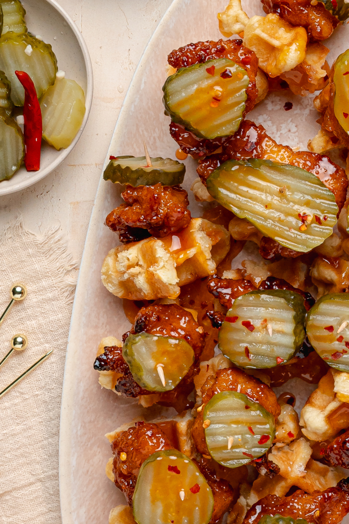 Hot Honey Peach Chicken and Waffle Bites Hot honey peach chicken and waffle bites topped with dill pickle chips and peach hot honey glaze on a serving platter.