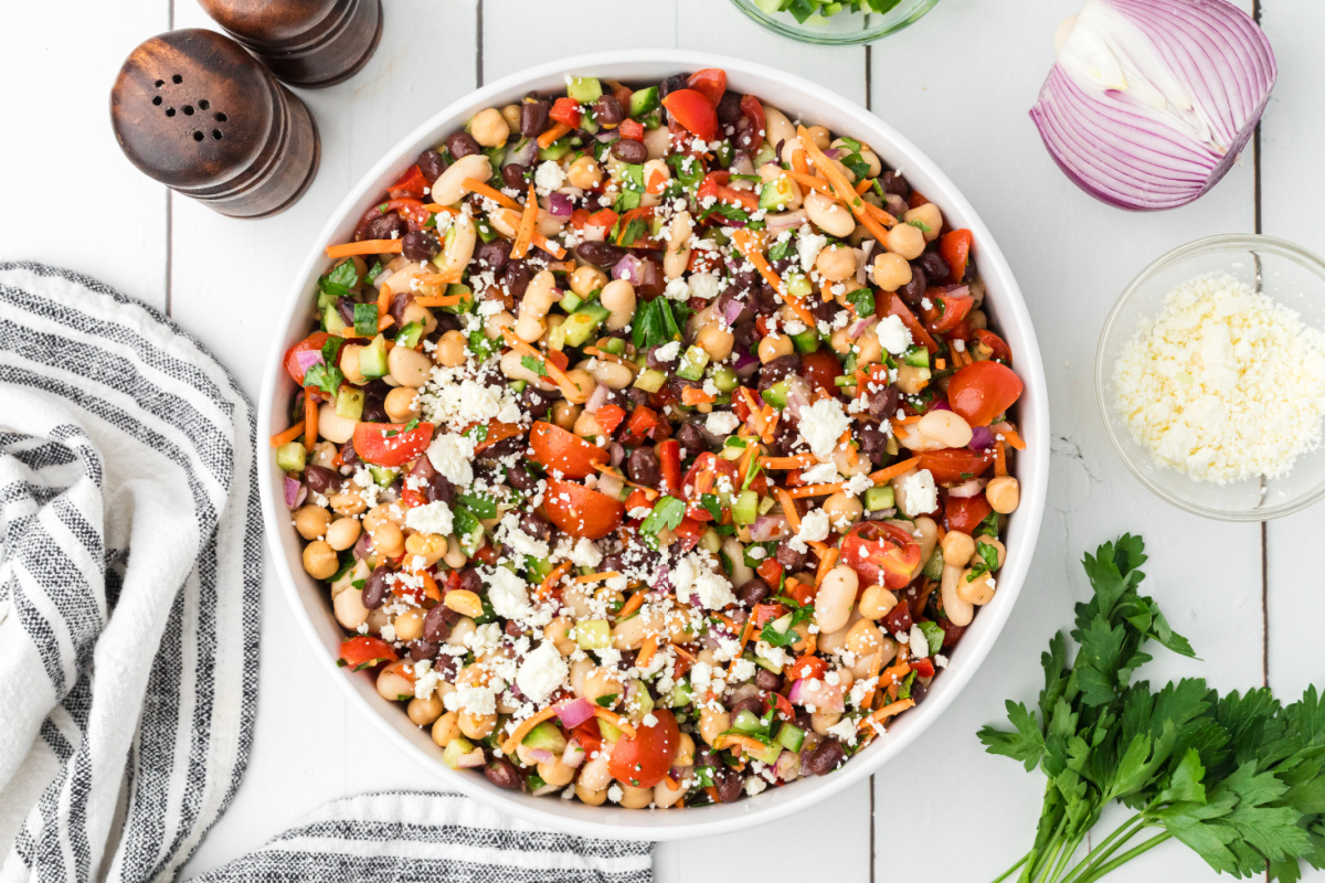 Overhead view of lemon Dijon dense bean salad tossed with chopped vegetables, feta cheese, and three kinds of beans. Lemon Dijon dense bean salad with black beans, chickpeas, cannellini beans, feta cheese, tomatoes, carrots, and cucumber