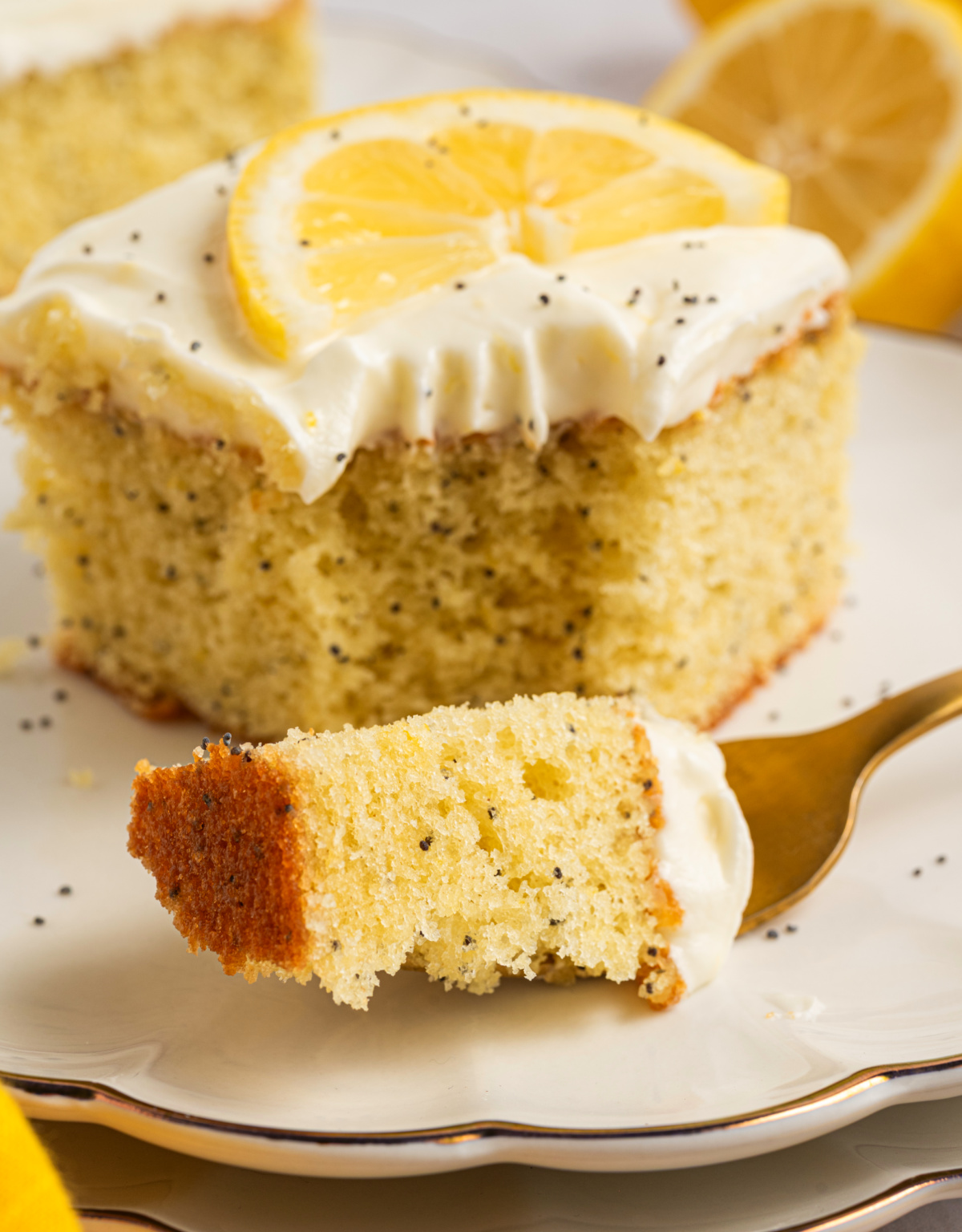 Close-up of lemon poppy seed cake with cream cheese frosting and a fork holding a bite, showing soft crumb and golden edges