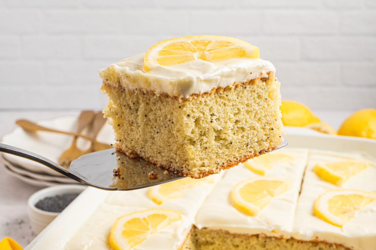 Fork lifting a slice of lemon poppy seed cake with cream cheese frosting, showing soft crumb and poppy seeds