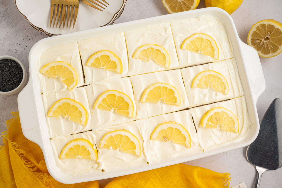 Lemon poppy seed sheet cake with cream cheese frosting, cut into squares and topped with lemon slices in a baking dish