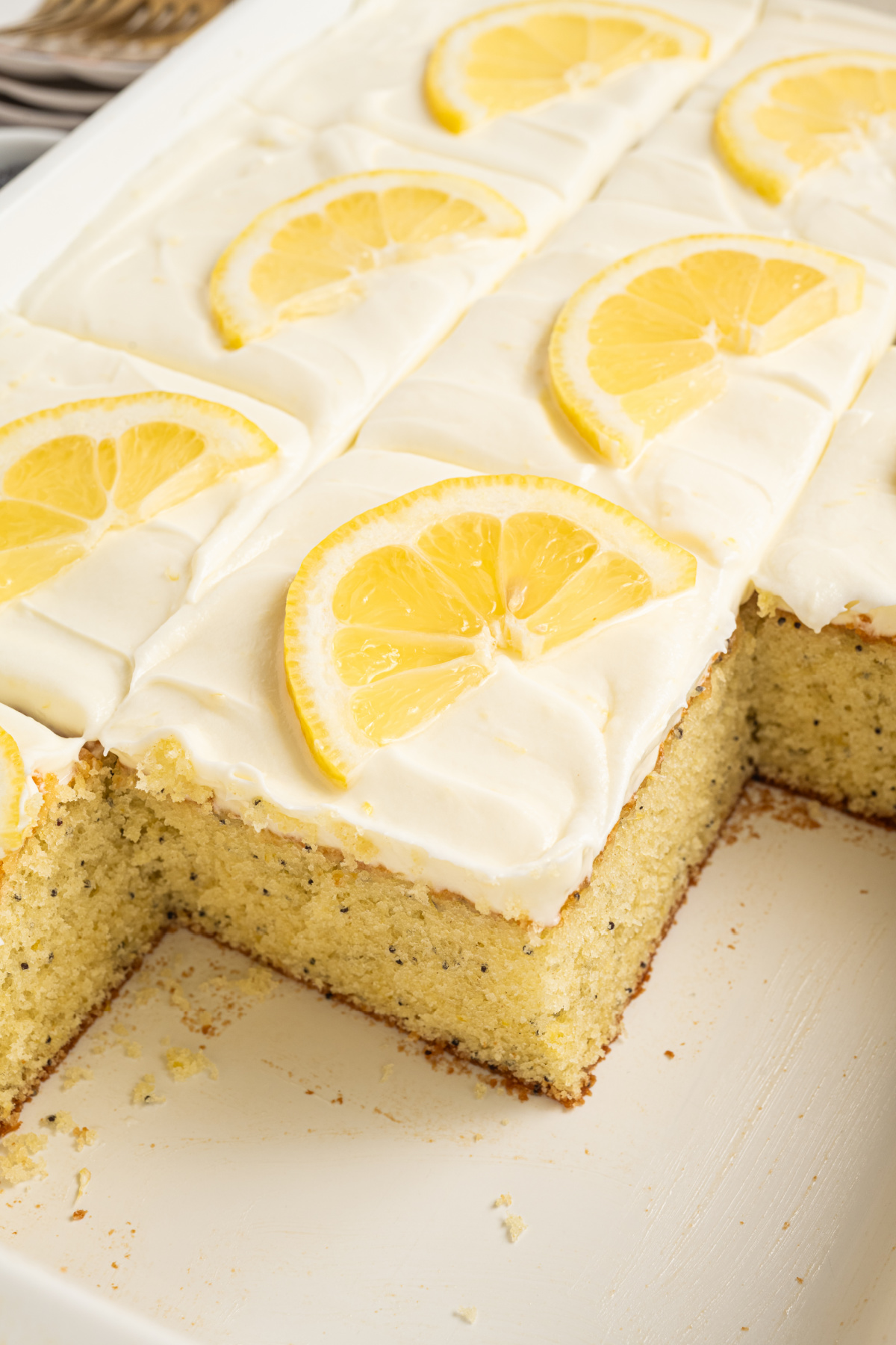 Close-up of lemon poppy seed sheet cake with cream cheese frosting, showing a cut corner and soft interior crumb