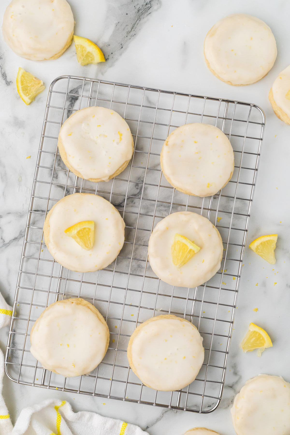 Lemon sugar cookies with lemon glaze cooling on a wire rack with fresh lemon wedges