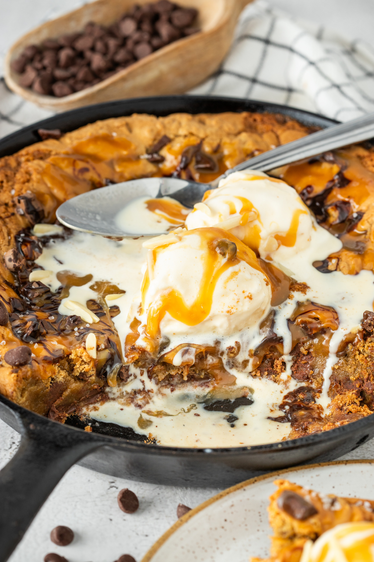 Molten center of a salted caramel skillet cookie with melting vanilla ice cream, chocolate chunks, caramel sauce, and crisp golden cookie edges in a cast iron skillet.