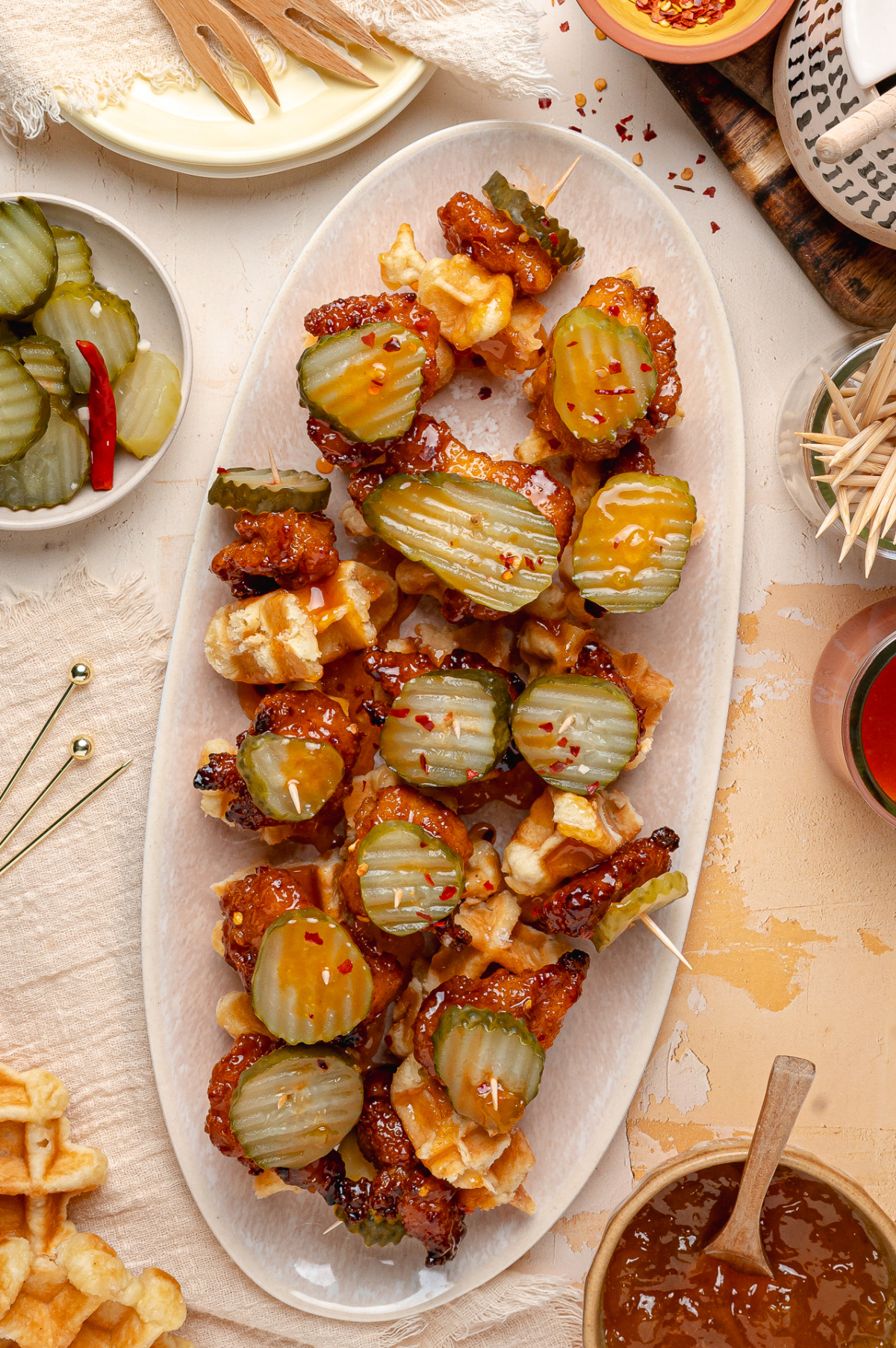 Peach Hot Honey Chicken Bites Platter Peach hot honey chicken bites arranged on waffle pieces with dill pickle chips and sticky glaze.