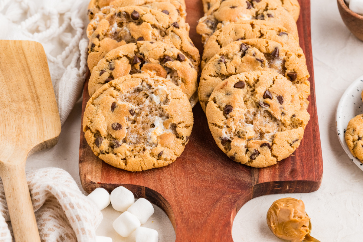 Bakery-Style Peanut Butter Cookies with Marshmallows Peanut butter marshmallow cookies arranged on a wooden serving board with visible toasted marshmallow pockets and mini chocolate chips.