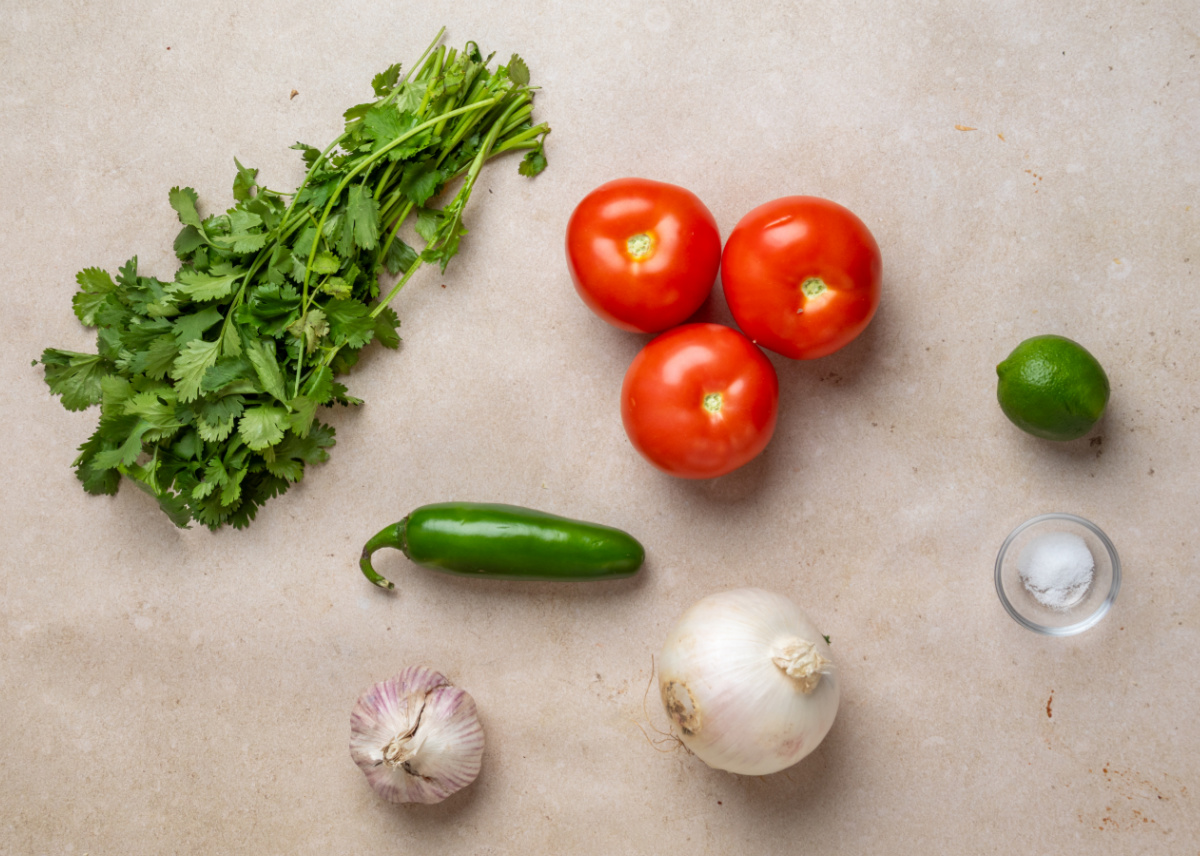 Fresh pico de gallo ingredients before chopping and mixing Ingredients for homemade pico de gallo including tomatoes, white onion, jalapeño, garlic, cilantro, lime, and salt