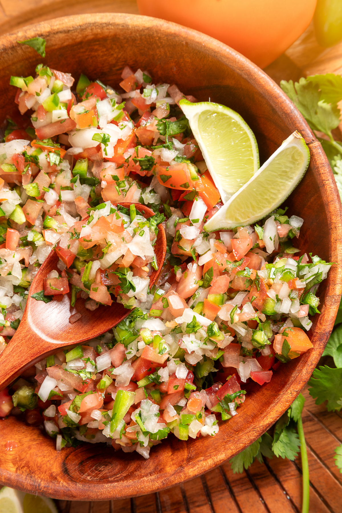 Fresh pico de gallo with lime wedges and chunky tomato texture Chunky pico de gallo with diced tomatoes, onion, jalapeño, cilantro, and lime wedges in a wooden bowl