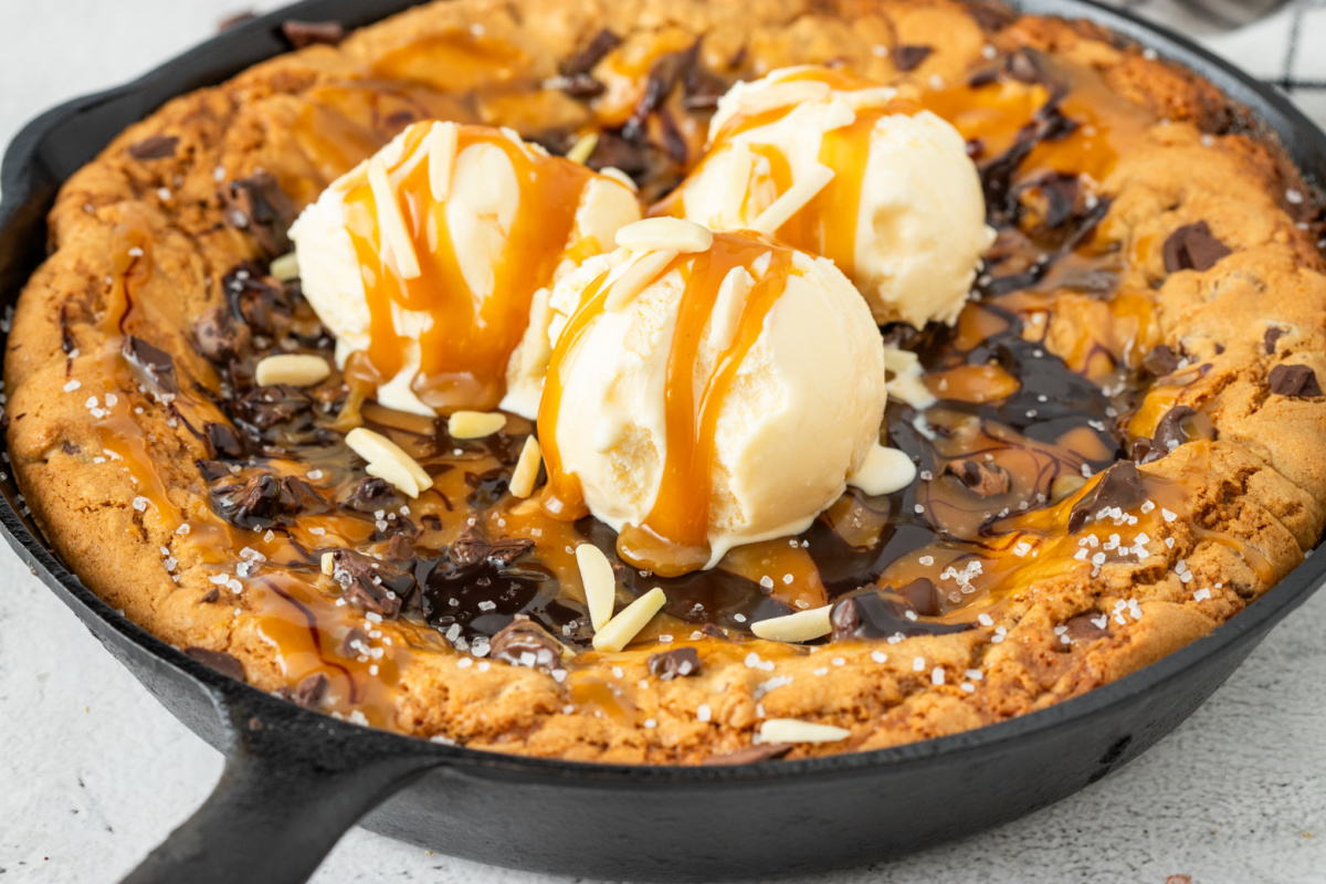 Salted caramel chocolate chip skillet cookie topped with vanilla ice cream, caramel sauce, melted chocolate, flaky sea salt, and chocolate chunks in a cast iron skillet.