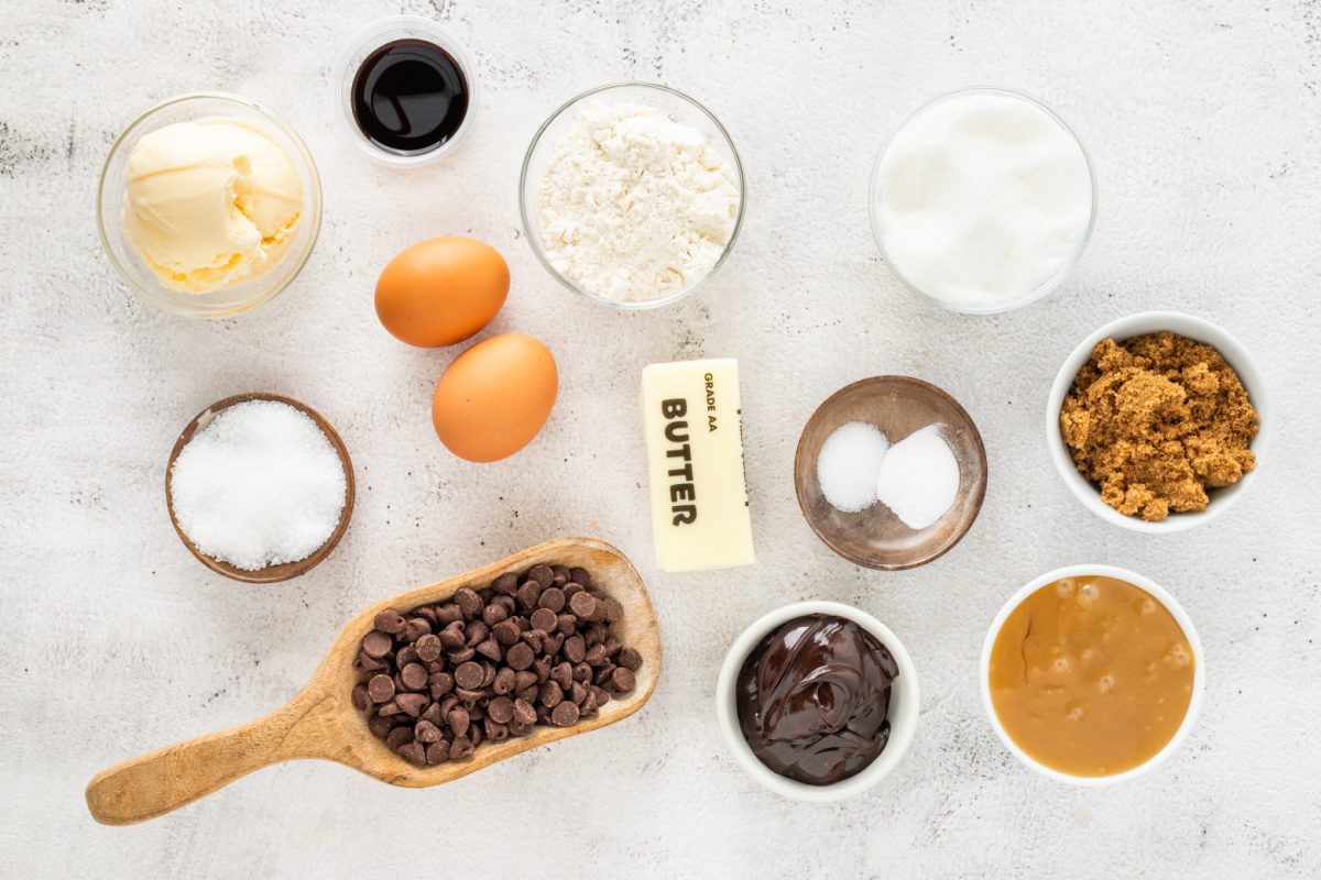 Ingredients for salted caramel chocolate chip skillet cookie including chocolate chips, salted caramel sauce, butter, brown sugar, eggs, flour, and flaky sea salt.