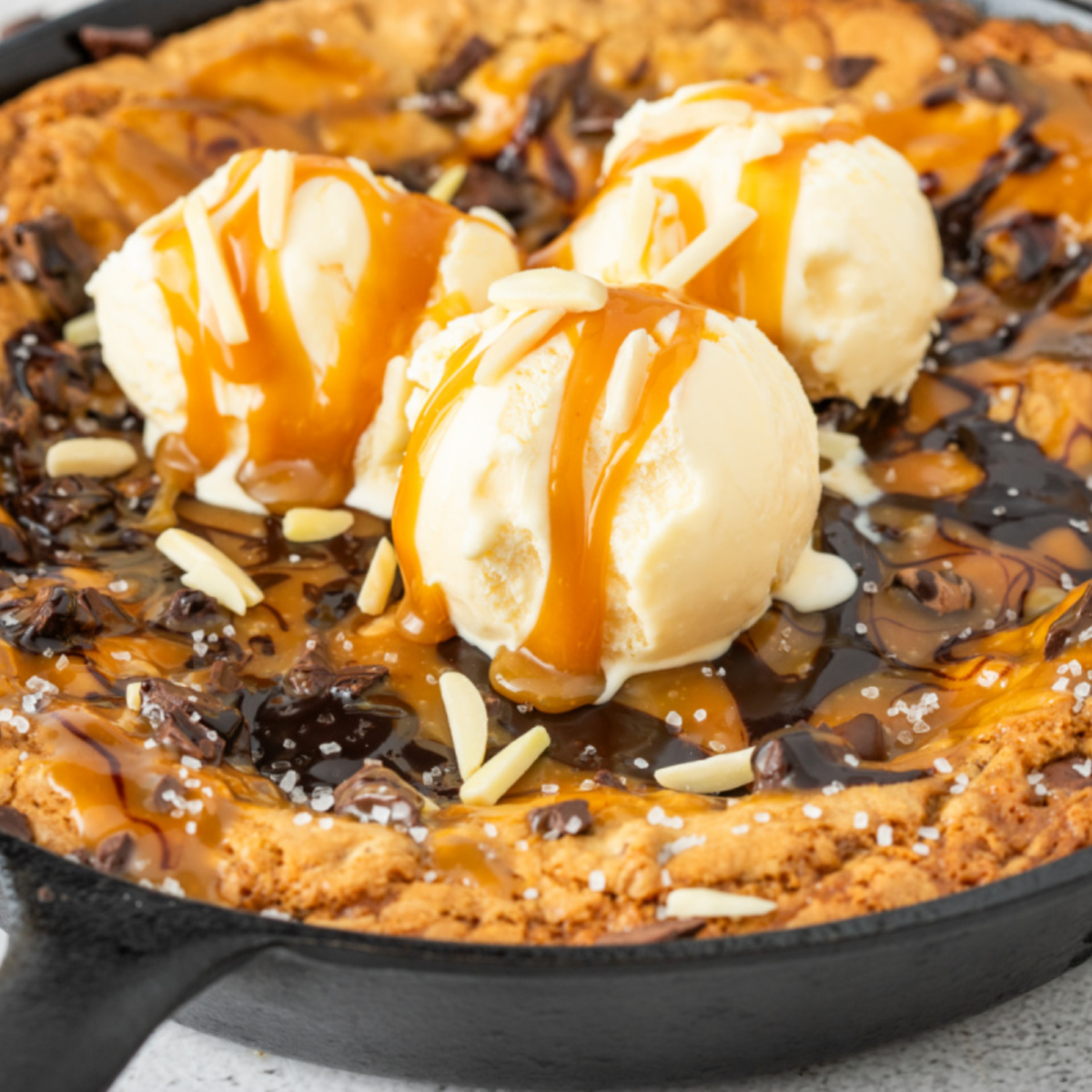 Warm salted caramel chocolate chip skillet cookie with molten caramel pockets, melted chocolate, crisp golden edges, and vanilla ice cream in a cast iron skillet.