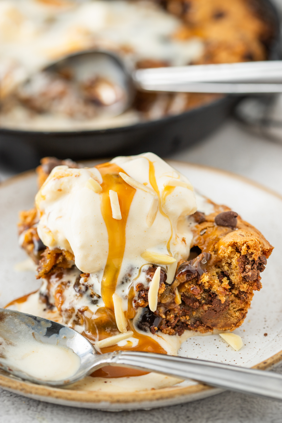 Slice of salted caramel skillet cookie topped with melting vanilla ice cream, caramel drizzle, chocolate chunks, and molten caramel on a dessert plate.