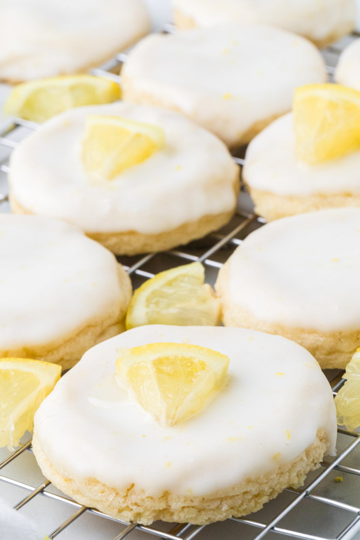 Soft lemon cookies with thick lemon glaze cooling on a wire rack with fresh lemon wedges