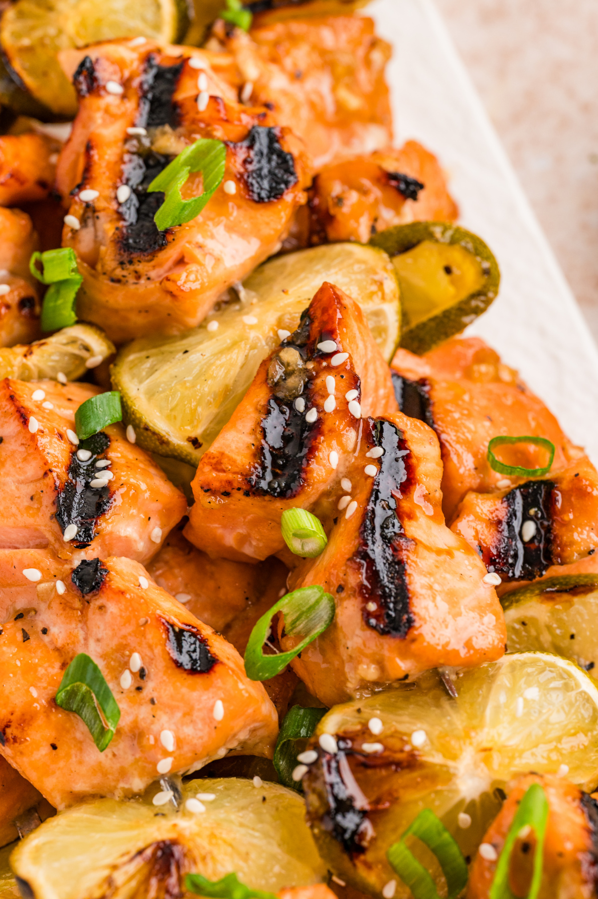 Close-up of soy lime salmon skewers with caramelized char, grilled lime slices, sesame seeds, and sliced green onions.