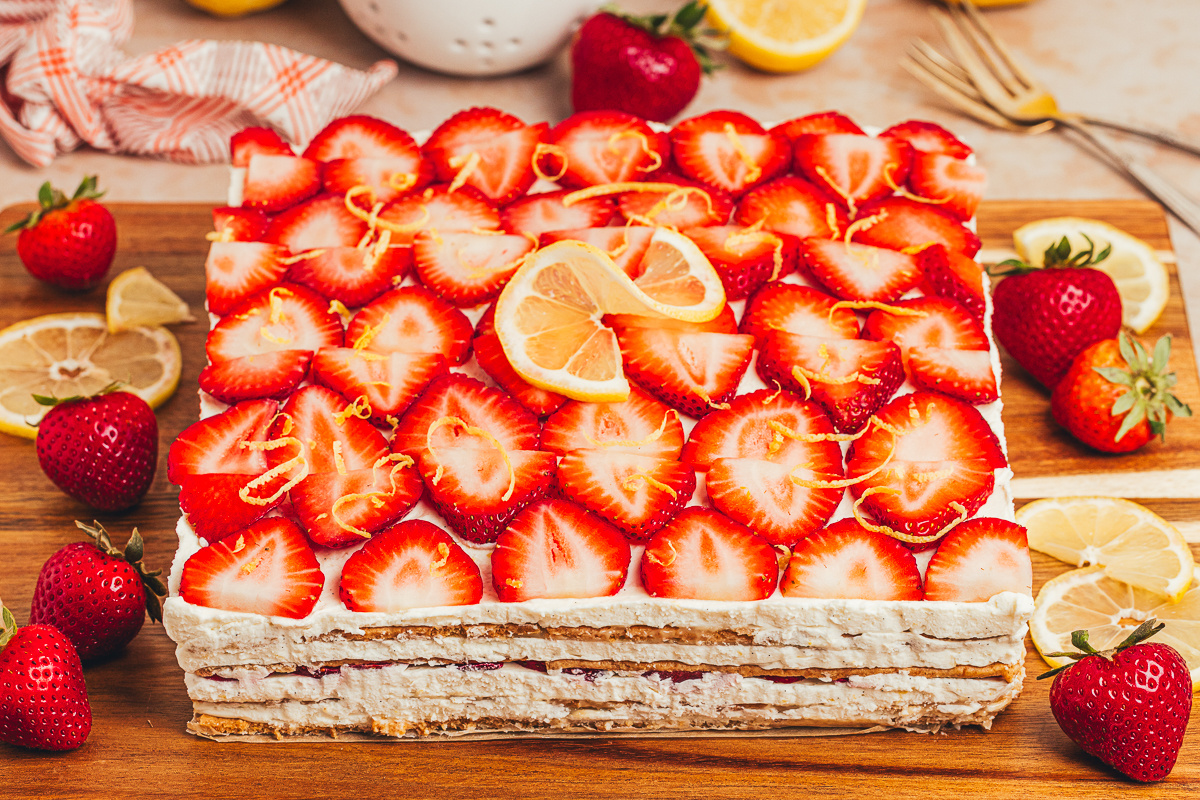 Whole strawberry lemon icebox cake topped with fresh strawberries, lemon slices, mascarpone cream, and graham cracker layers.