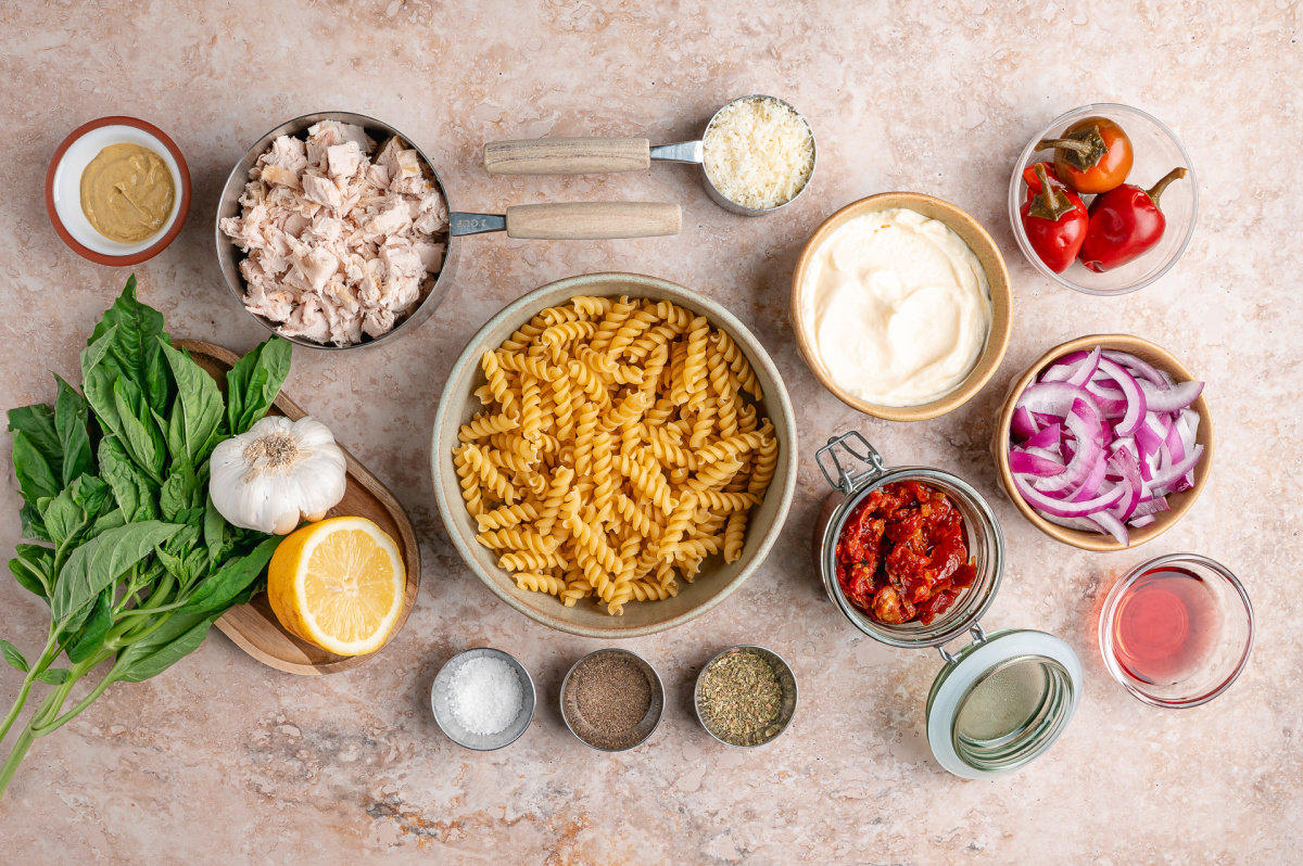 Ingredients for Sun-Dried Tomato Chicken Pasta Salad including rotini pasta, rotisserie chicken, basil, lemon, Parmesan, mayonnaise, and oil-packed sun-dried tomatoes