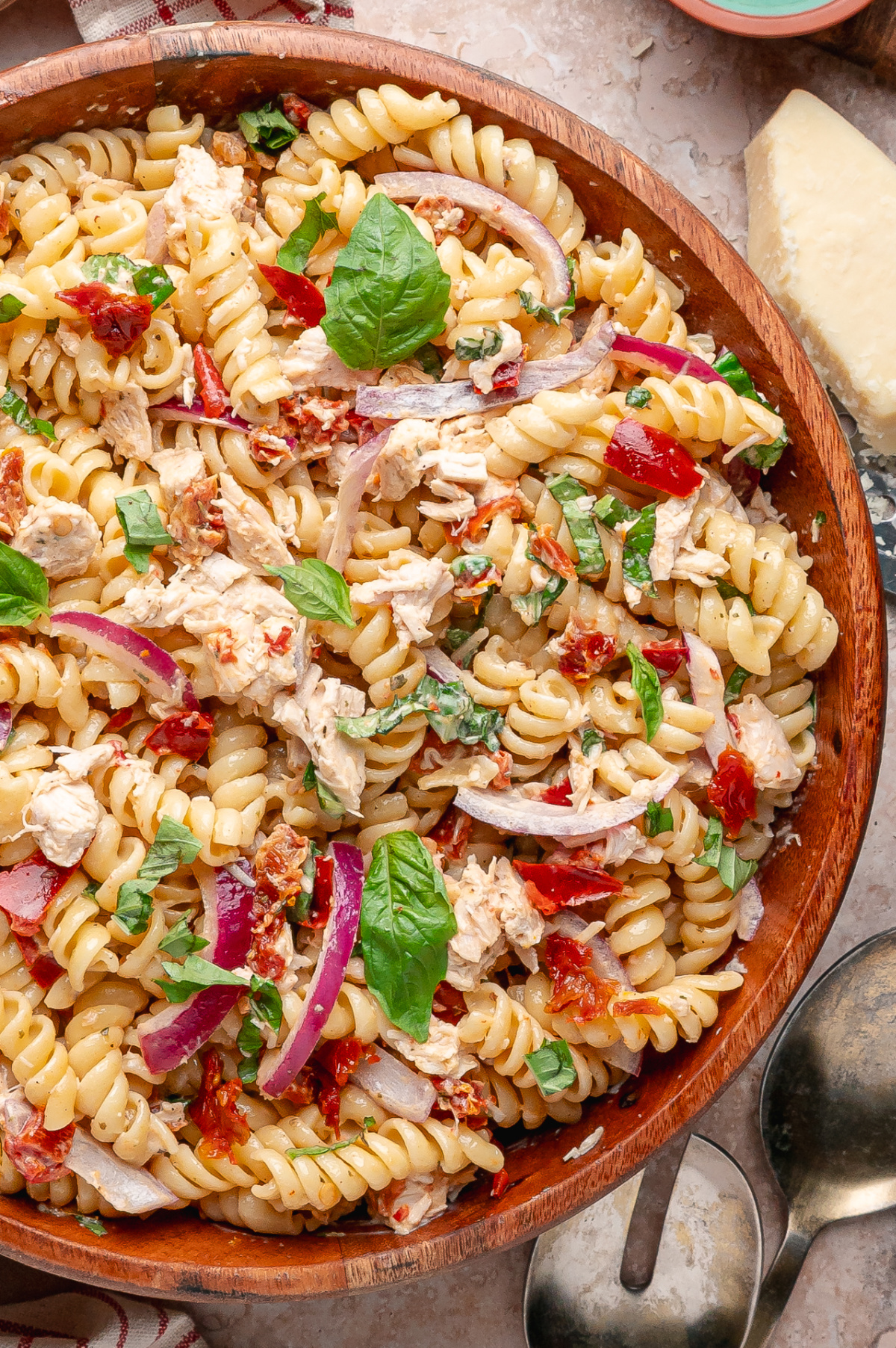 Sun-Dried Tomato Chicken Pasta Salad with rotini, rotisserie chicken, basil, red onion, roasted red peppers, and Parmesan in a wooden serving bowl