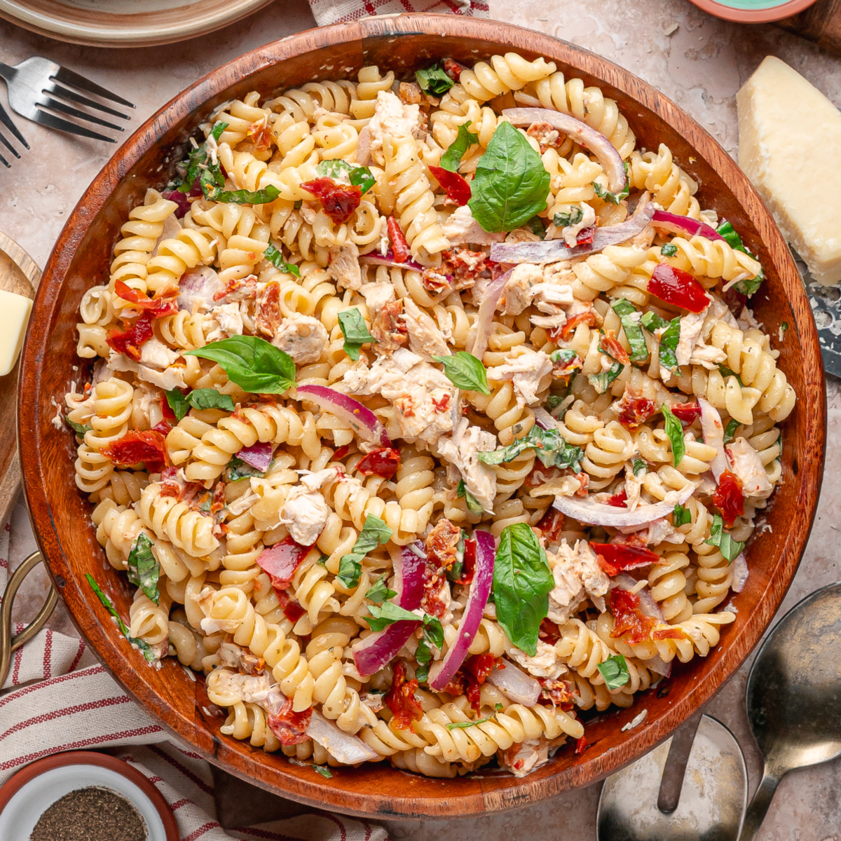 Sun-Dried Tomato Chicken Pasta Salad with rotini, rotisserie chicken, basil, red onion, Parmesan, and chopped sun-dried tomatoes in a wooden serving bowl