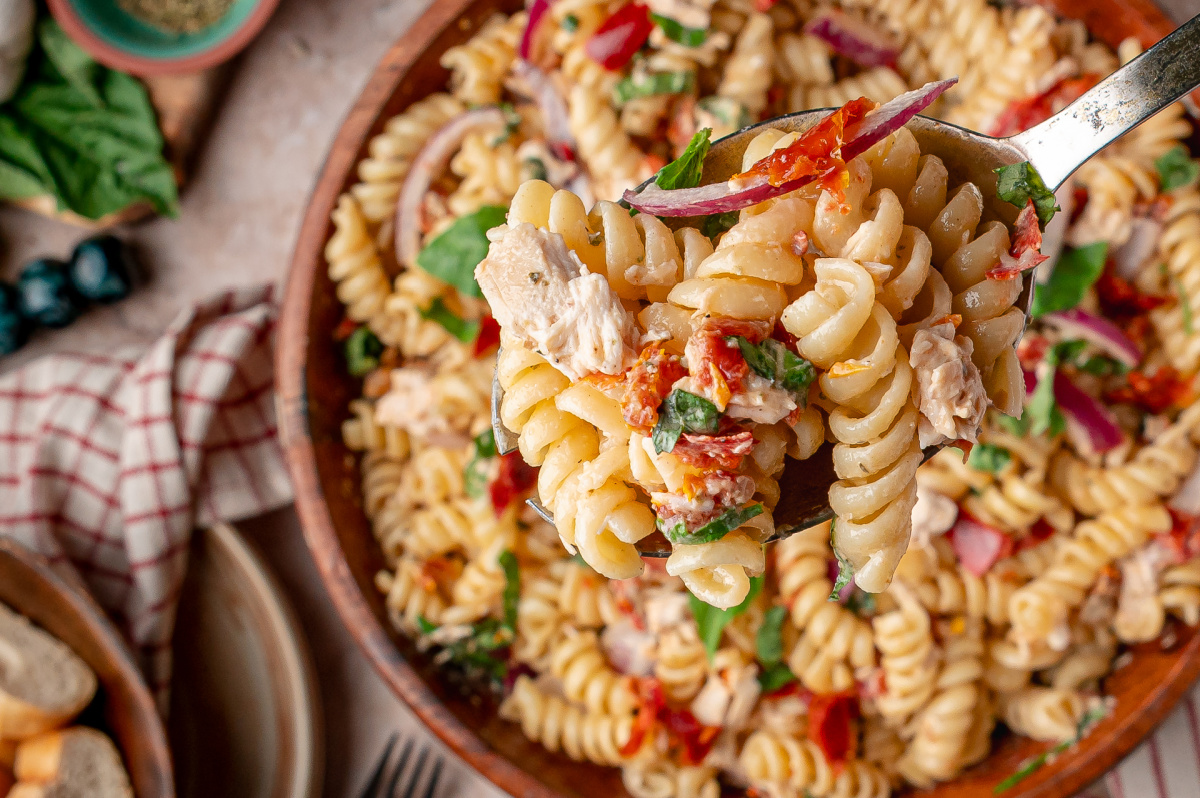 Spoonful of Sun-Dried Tomato Chicken Pasta Salad with rotini, rotisserie chicken, basil, and red onion over a serving bowl
