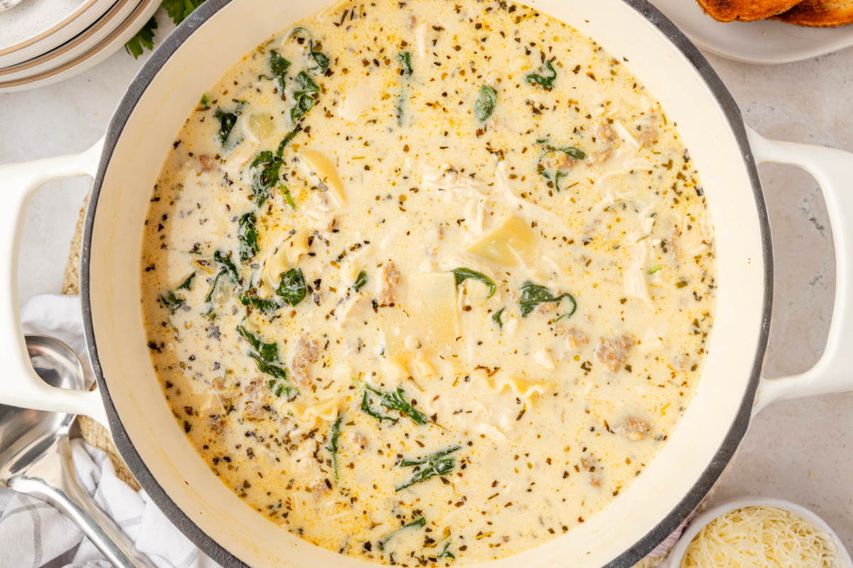 White Lasagna Soup simmering with ricotta, sausage, spinach, and lasagna noodles White Lasagna Soup with spinach, sausage, chicken, ricotta, and broken lasagna noodles simmering in a Dutch oven
