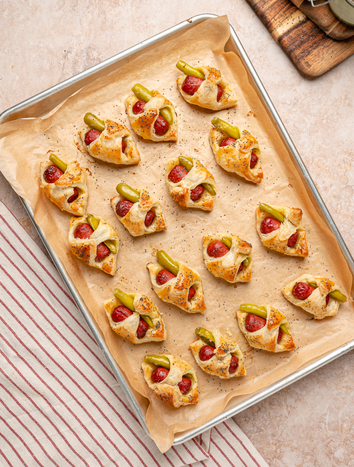 Freshly baked Chicago hot dog pigs in a blanket on a parchment-lined sheet pan.