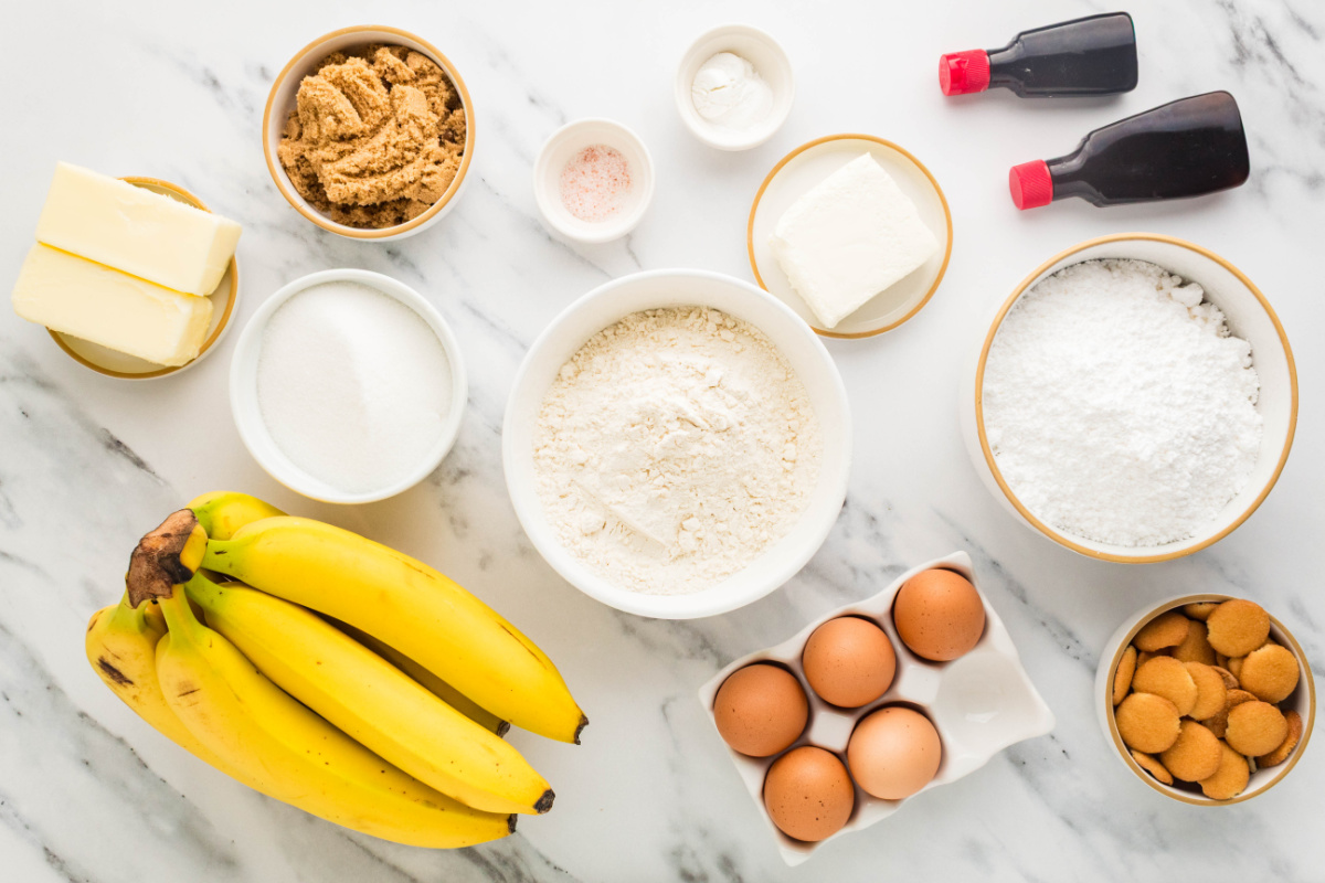 Ingredients for banana pudding cookies including ripe bananas, instant banana pudding mix, flour, butter, sugars, eggs, cream cheese, confectioners' sugar, vanilla, baking powder, sea salt, and vanilla wafers.