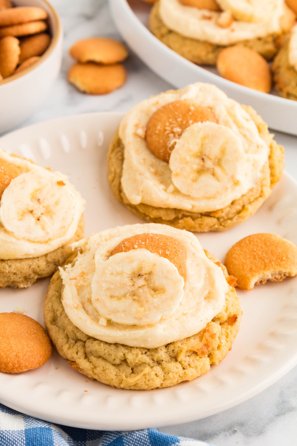 Banana pudding cookies served on a plate with brown butter cream cheese frosting, mini vanilla wafers, and fresh banana slices.