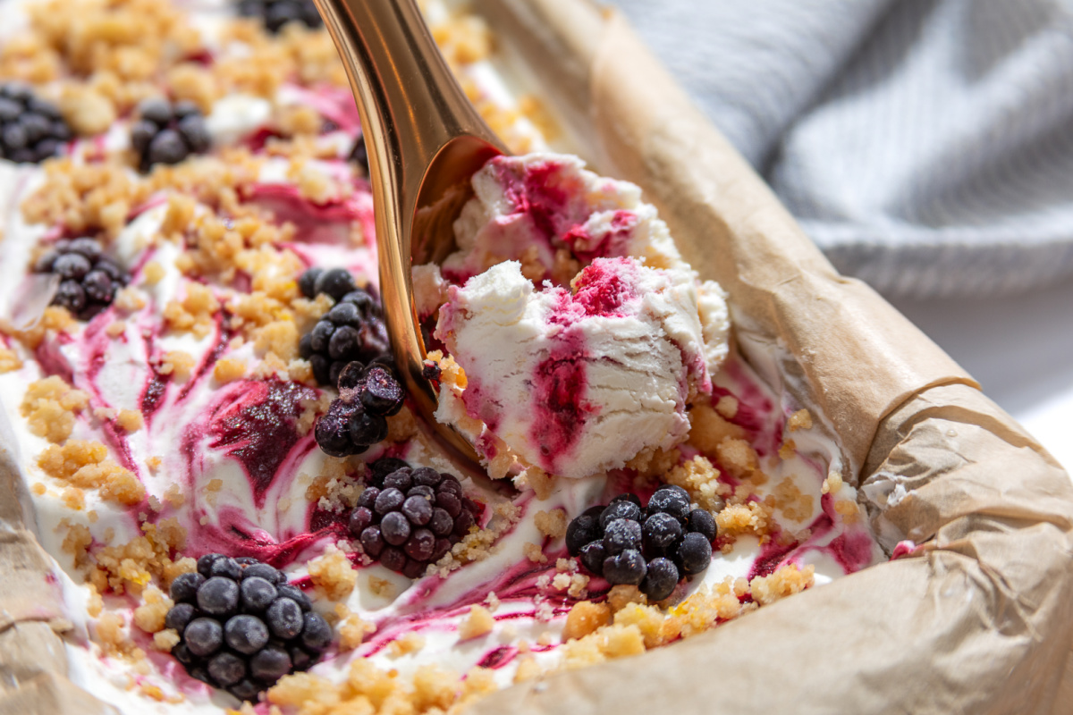 Every scoop of Blackberry Crumble à la Mode Ice Cream has thick blackberry swirls and buttery shortbread crumble. A scoop of Blackberry Crumble à la Mode Ice Cream with thick blackberry ribbons and buttery shortbread crumble being lifted from the loaf pan.