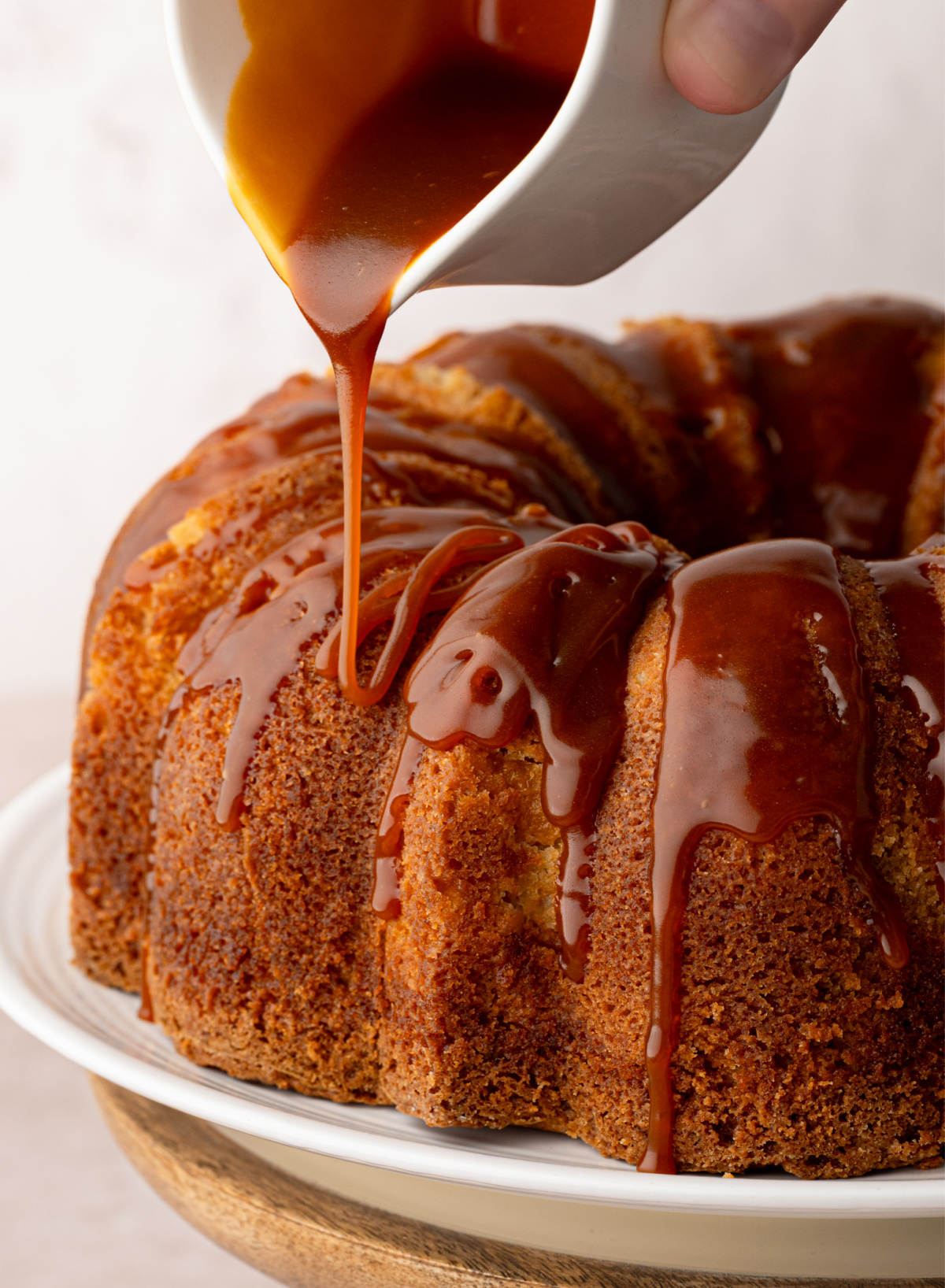 Warm bourbon caramel being poured over peach cobbler Bundt cake. Pouring bourbon caramel over peach cobbler Bundt cake before serving.
