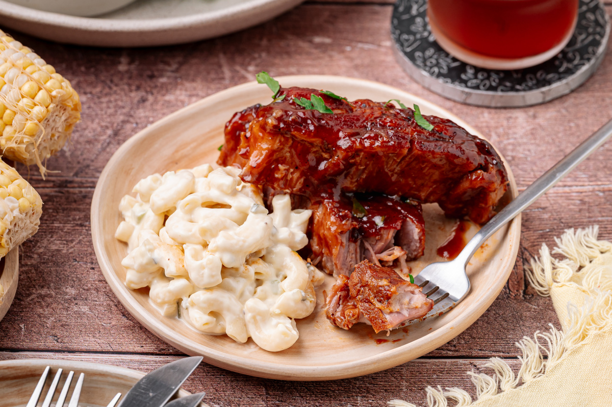 A serving of bourbon peach country style ribs with a sticky peach barbecue glaze and creamy macaroni salad. Bourbon peach country style ribs with peach barbecue glaze served with macaroni salad