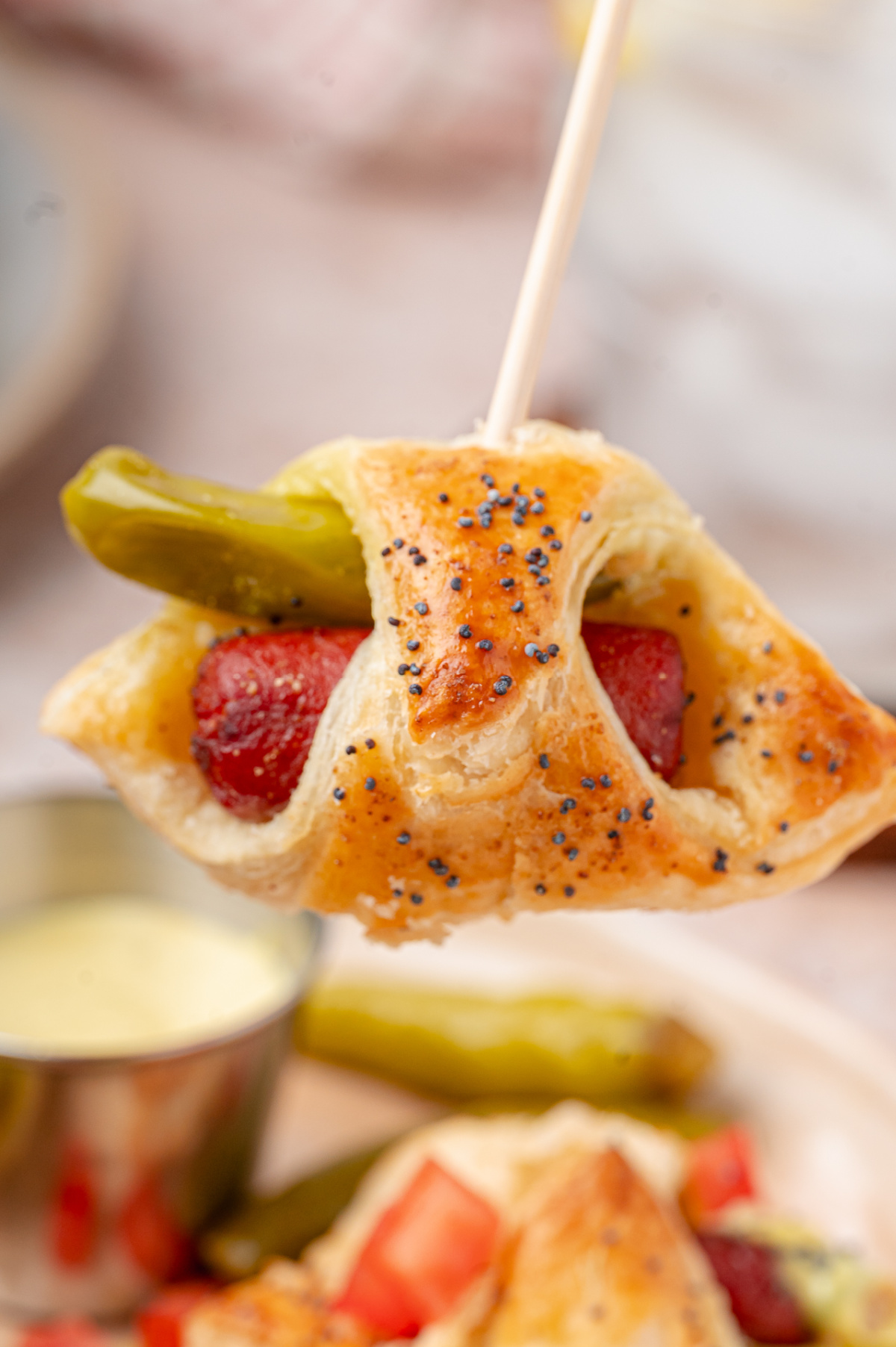 A party-ready Chicago hot dog pig in a blanket with flaky puff pastry, a beef cocktail frank, and a sport pepper. Chicago hot dog pigs in a blanket with a sport pepper and beef cocktail frank held on a toothpick.
