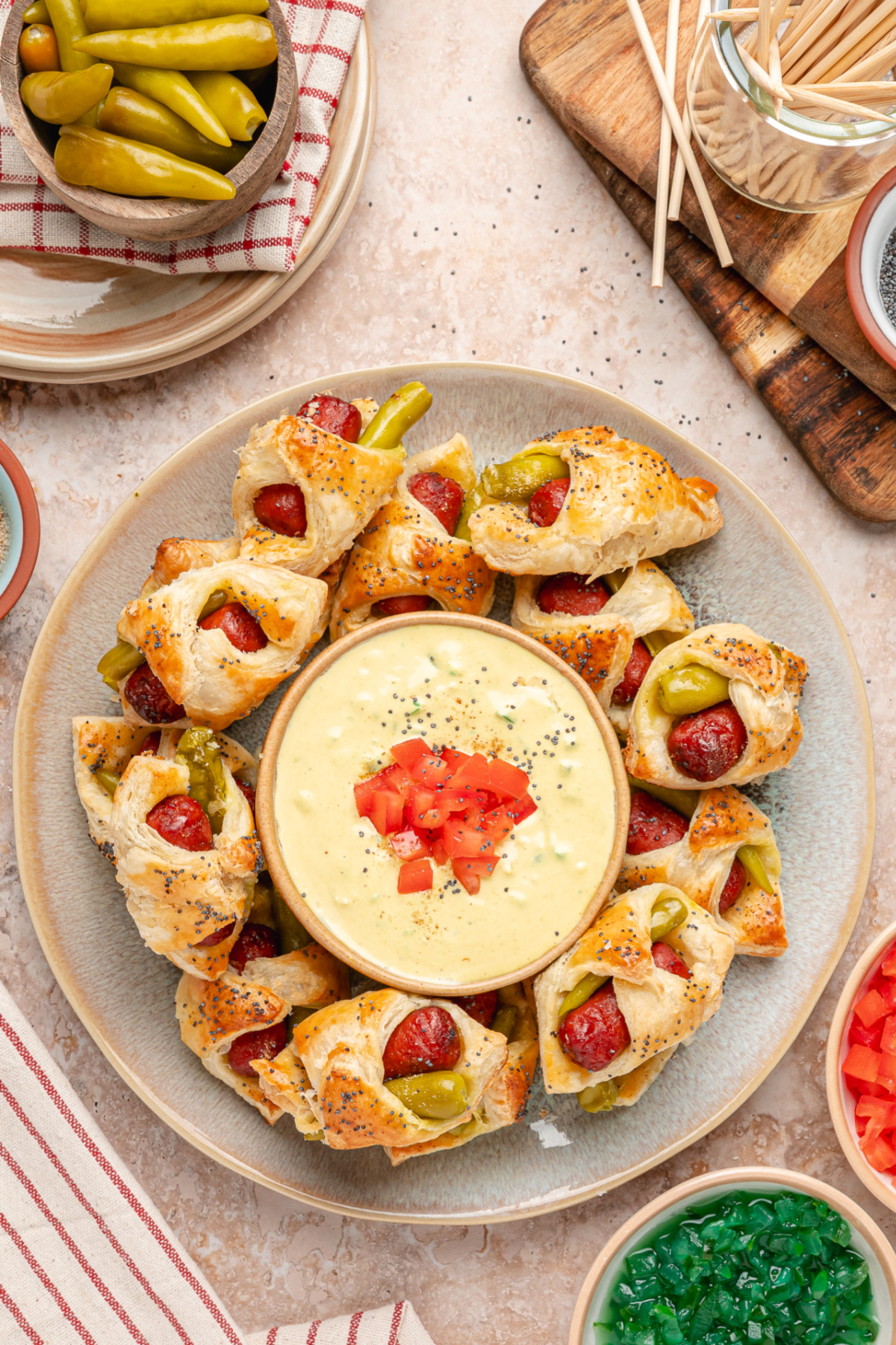 Flaky Chicago hot dog pigs in a blanket served with a creamy mustard relish dip inspired by the classic Chicago dog. Chicago hot dog pigs in a blanket arranged around a creamy mustard relish dip topped with fresh tomato.