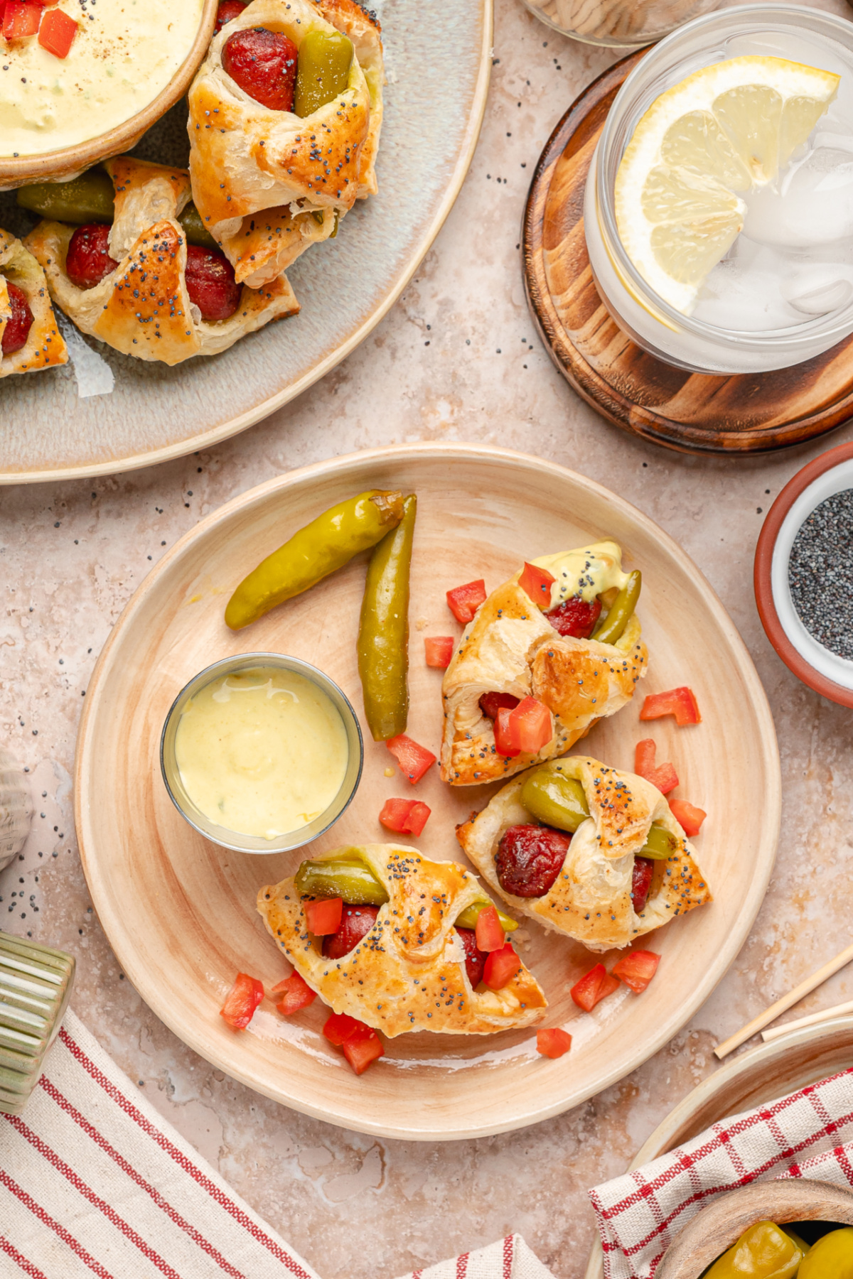A serving plate of Chicago hot dog pigs in a blanket with sport peppers and creamy mustard relish dip. Chicago hot dog pigs in a blanket served with mustard relish dip, sport peppers, and diced tomato.