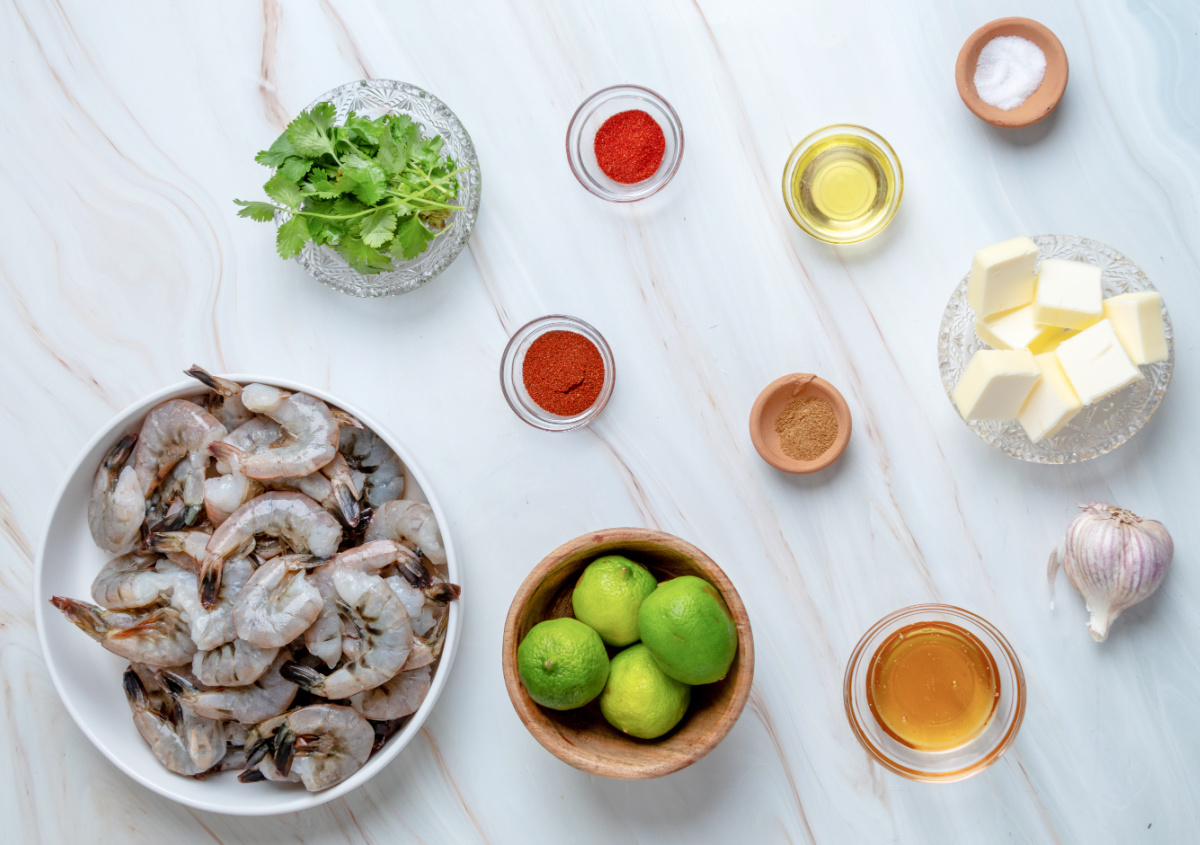 Ingredients for chipotle honey grilled shrimp skewers including shrimp, hot honey, butter, garlic, lime, cilantro, and spices