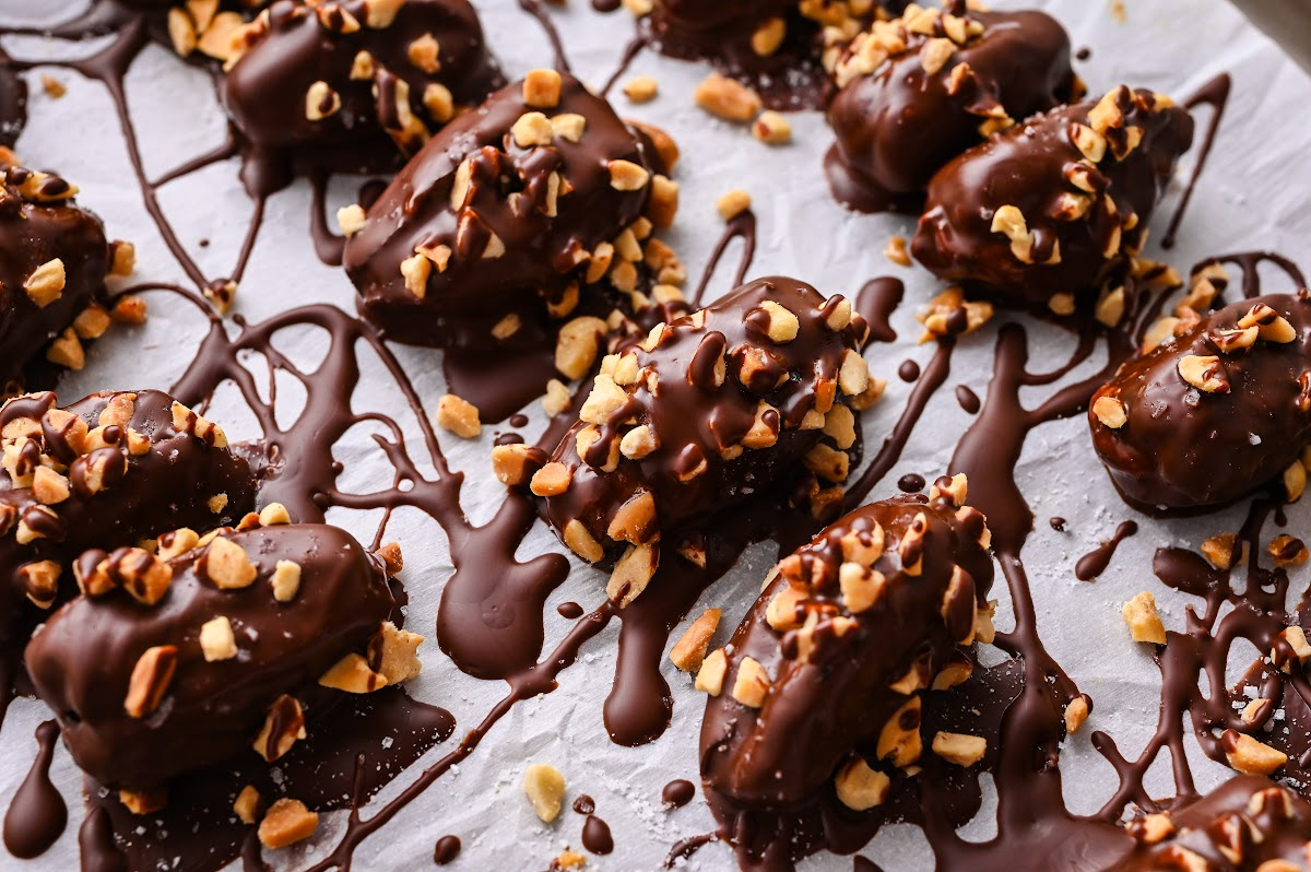 Close-up of chocolate peanut butter stuffed dates topped with chopped peanuts Chocolate peanut butter stuffed dates coated in dark chocolate with chopped peanuts and extra chocolate drizzle