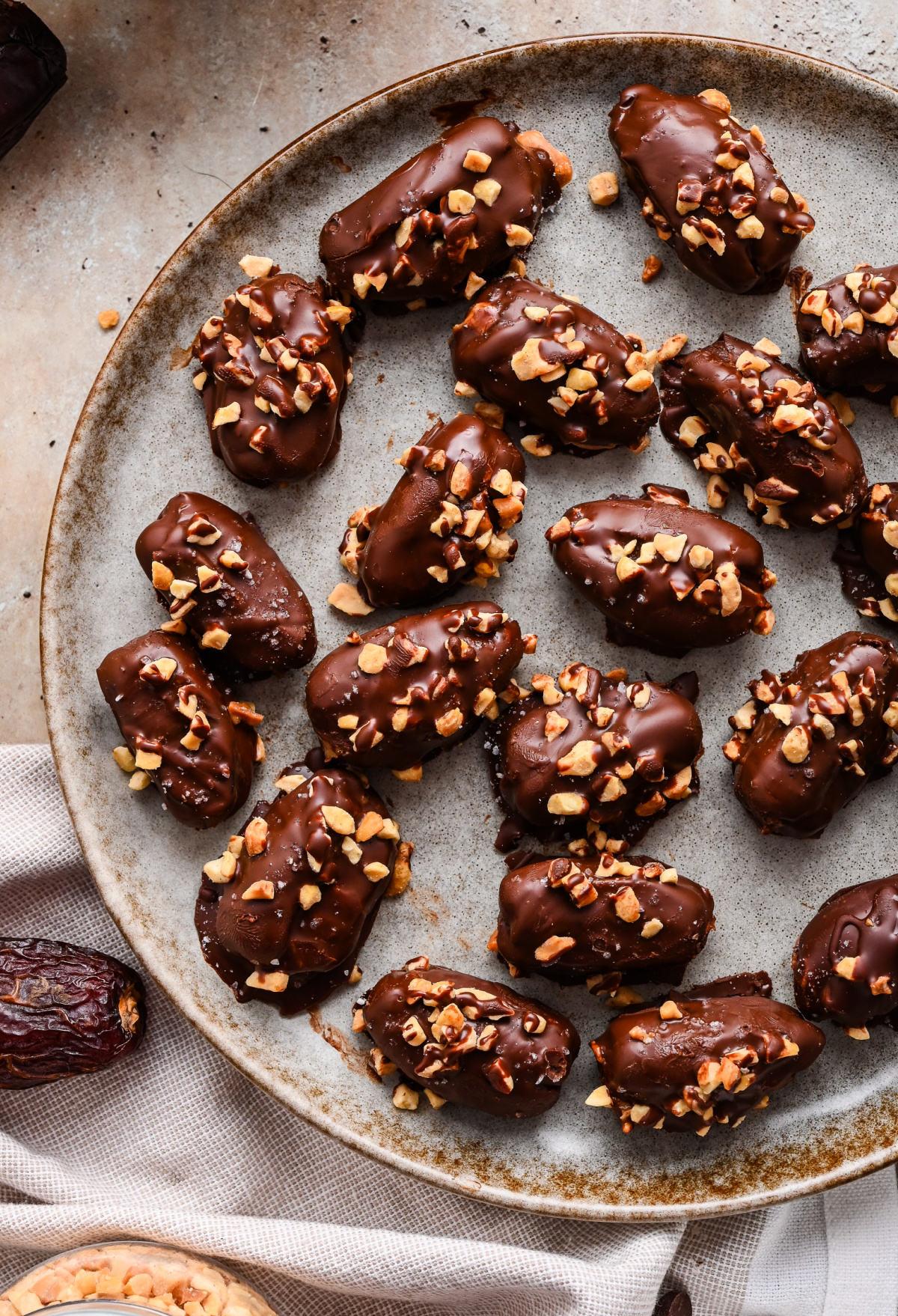 Chocolate peanut butter stuffed dates with dark chocolate, chopped peanuts, and flaky sea salt Chocolate peanut butter stuffed dates coated in dark chocolate and topped with chopped peanuts on a serving platter