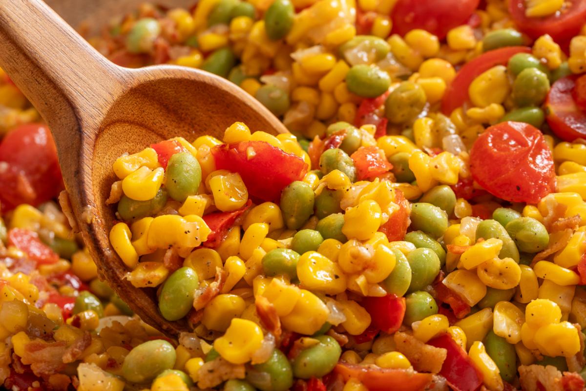 Close-up spoonful of corn succotash with edamame, tomatoes, bacon, and sweet corn