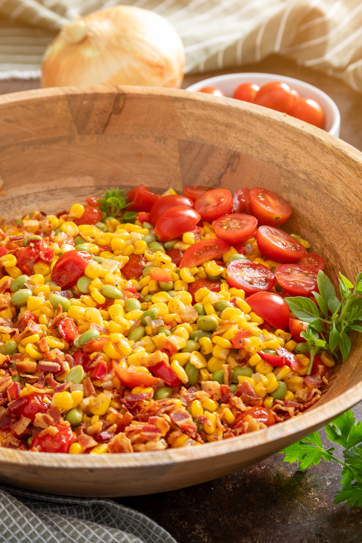 Corn succotash with edamame, bacon, tomatoes, peppers, and sweet corn in a wooden serving bowl