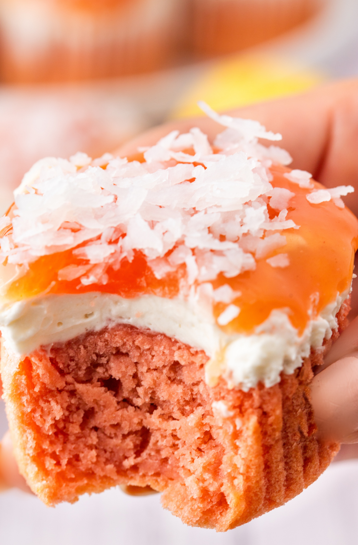 Inside of a guava cream cheese cupcake showing the pink cake, cream cheese layer, guava glaze, and coconut