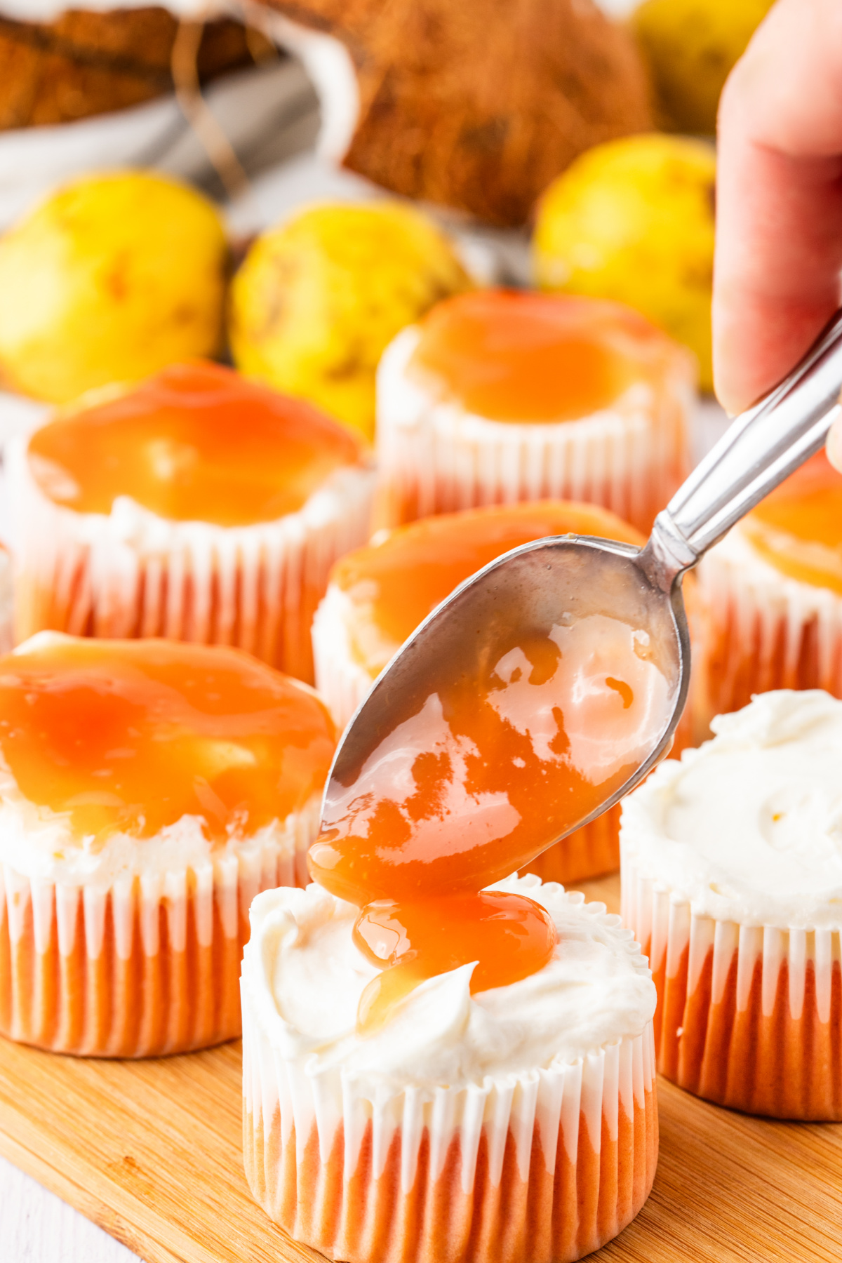 Spooning guava glaze over cream cheese topped cupcakes before adding coconut