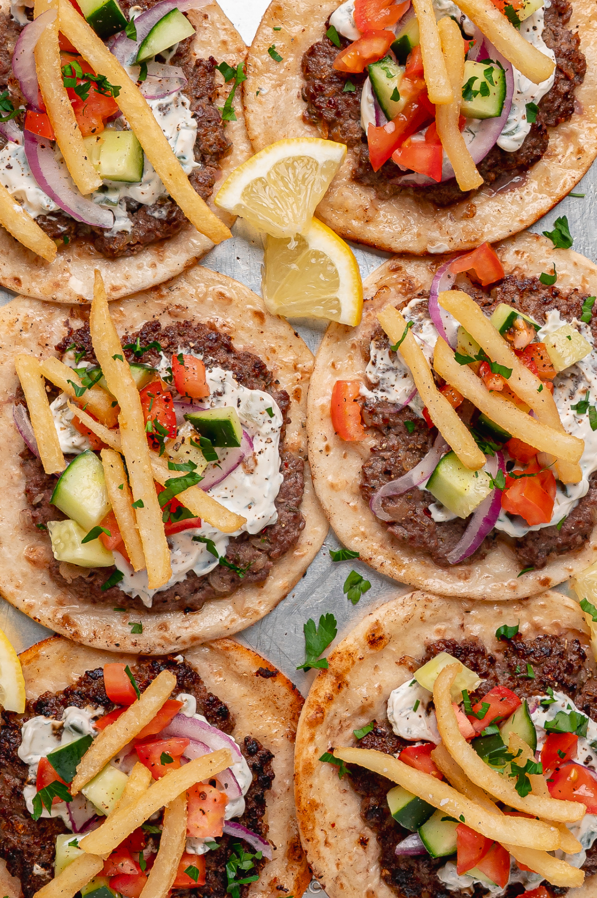 A close look at gyro smashed tacos with crispy beef, fresh vegetables, tzatziki, and fries. Gyro smashed tacos topped with tzatziki, fries, cucumber, tomato, and red onion in a close-up overhead view.