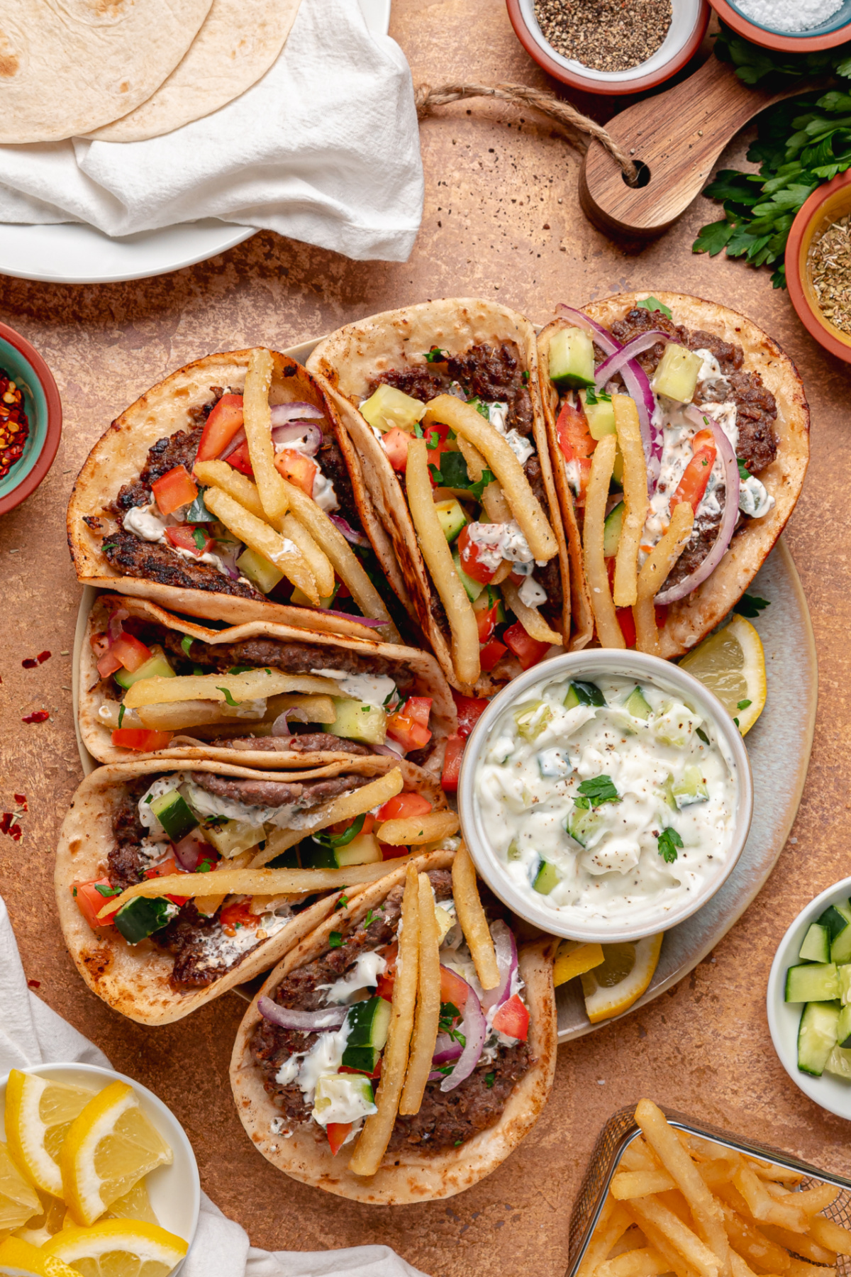 Gyro smashed tacos loaded with seasoned beef, tzatziki, fresh vegetables, and fries. Gyro smashed tacos topped with tzatziki, fries, cucumber, tomato, and red onion served on a platter.
