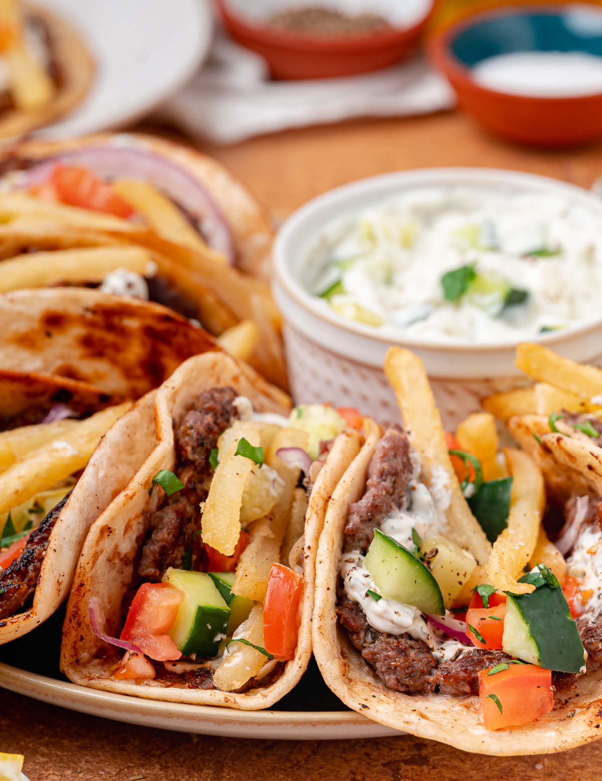 A close-up of gyro tacos loaded with crispy beef, cool tzatziki, fresh vegetables, and fries. Gyro tacos with tzatziki, fries, cucumber, tomato, and red onion served on a platter.