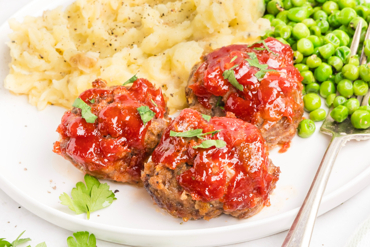 Mini meatloaf recipe fresh from the oven in a muffin tin Mini meatloaf recipe with tomato glaze served with mashed potatoes and peas
