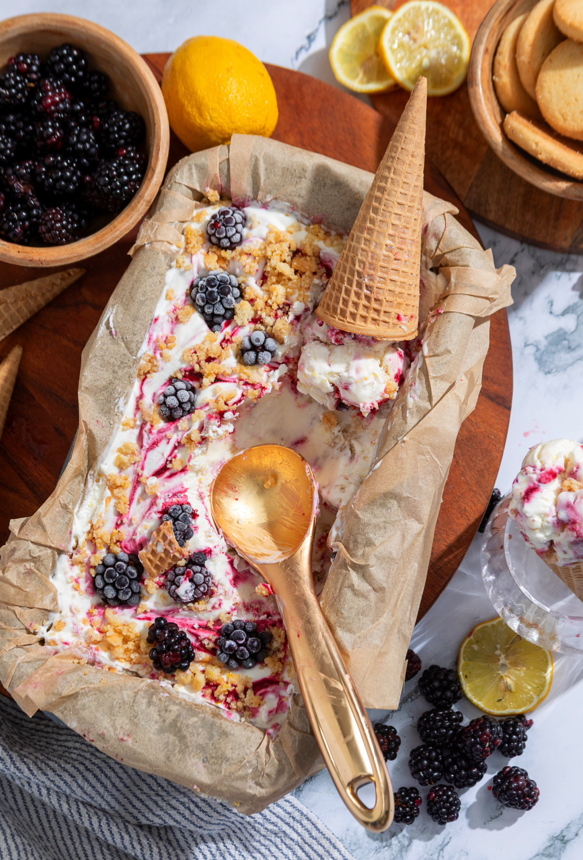 Serve this homemade no-churn blackberry ice cream straight from the loaf pan with waffle cones and extra blackberry crumble. A loaf pan of homemade no-churn blackberry ice cream with blackberry swirls, shortbread crumble, fresh blackberries, and waffle cones.