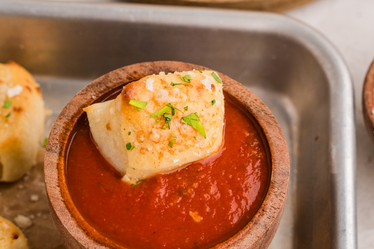 A Parmesan bread bite ready for dipping in marinara sauce Parmesan bread bite dipped in marinara sauce and topped with Parmesan cheese and parsley
