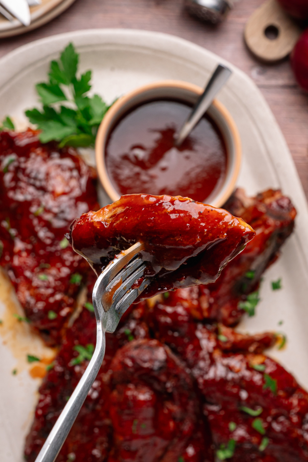 A tender country style pork rib coated in peach bourbon glaze and lifted from the serving platter. Fork lifting a peach bourbon glazed country style rib over a platter of ribs with sauce in a bowl